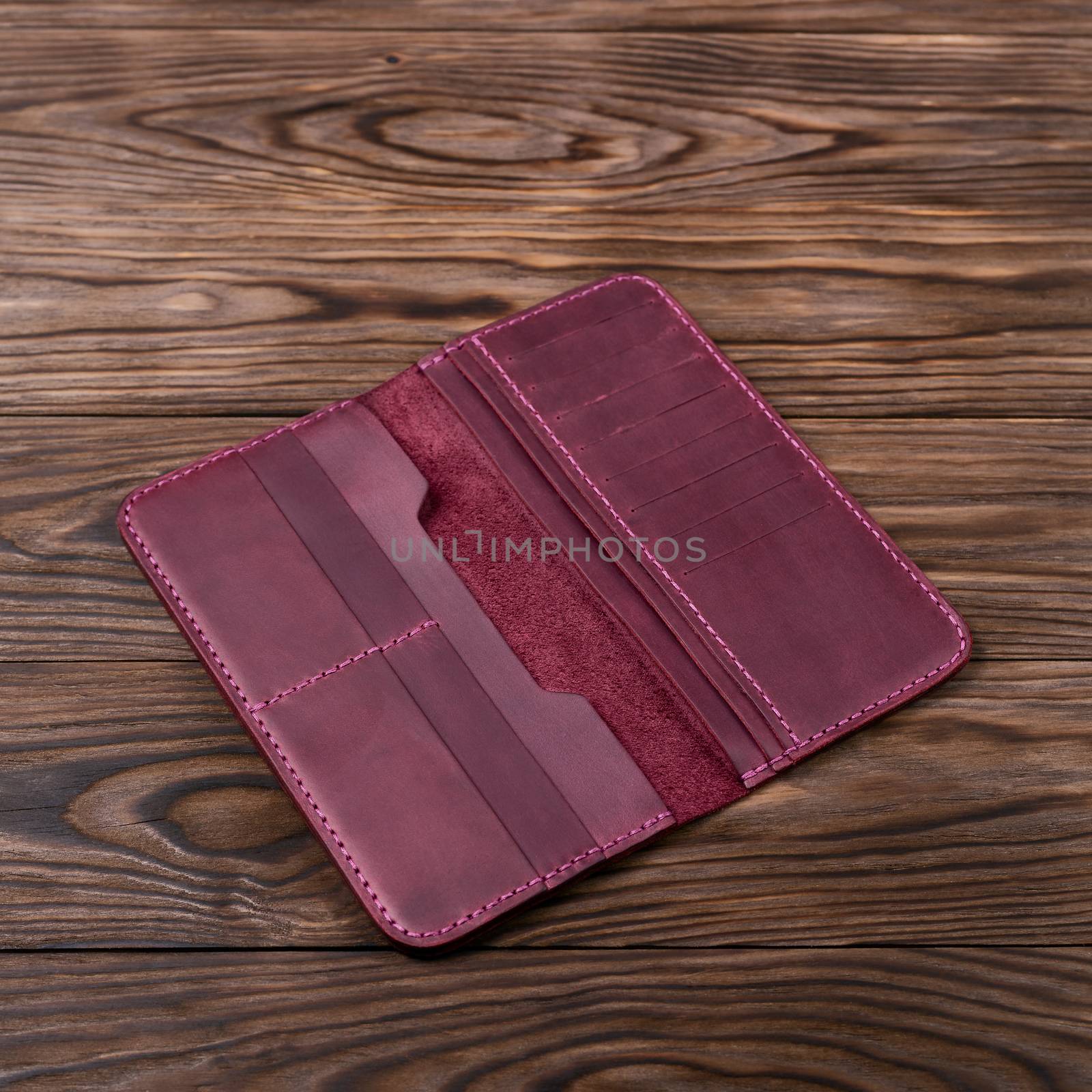 Purple color handmade leather porte-monnaie on wooden textured background. Purse is opened and empty. Side view. Stock photo of luxury accessories.