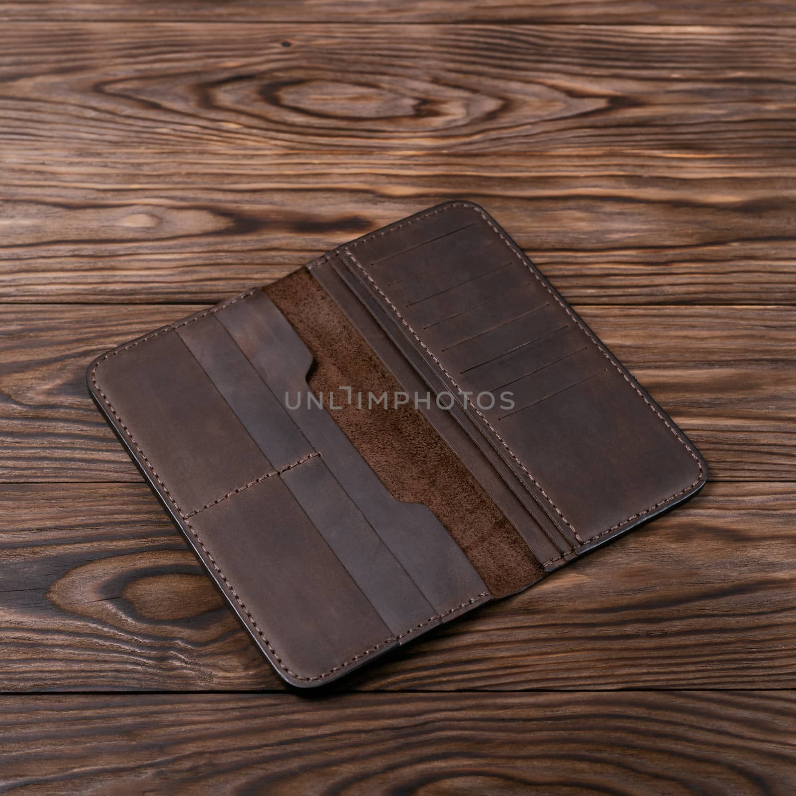 Brown color handmade leather porte-monnaie on wooden textured background. Purse is opened and empty. Side view. Stock photo of luxury accessories.