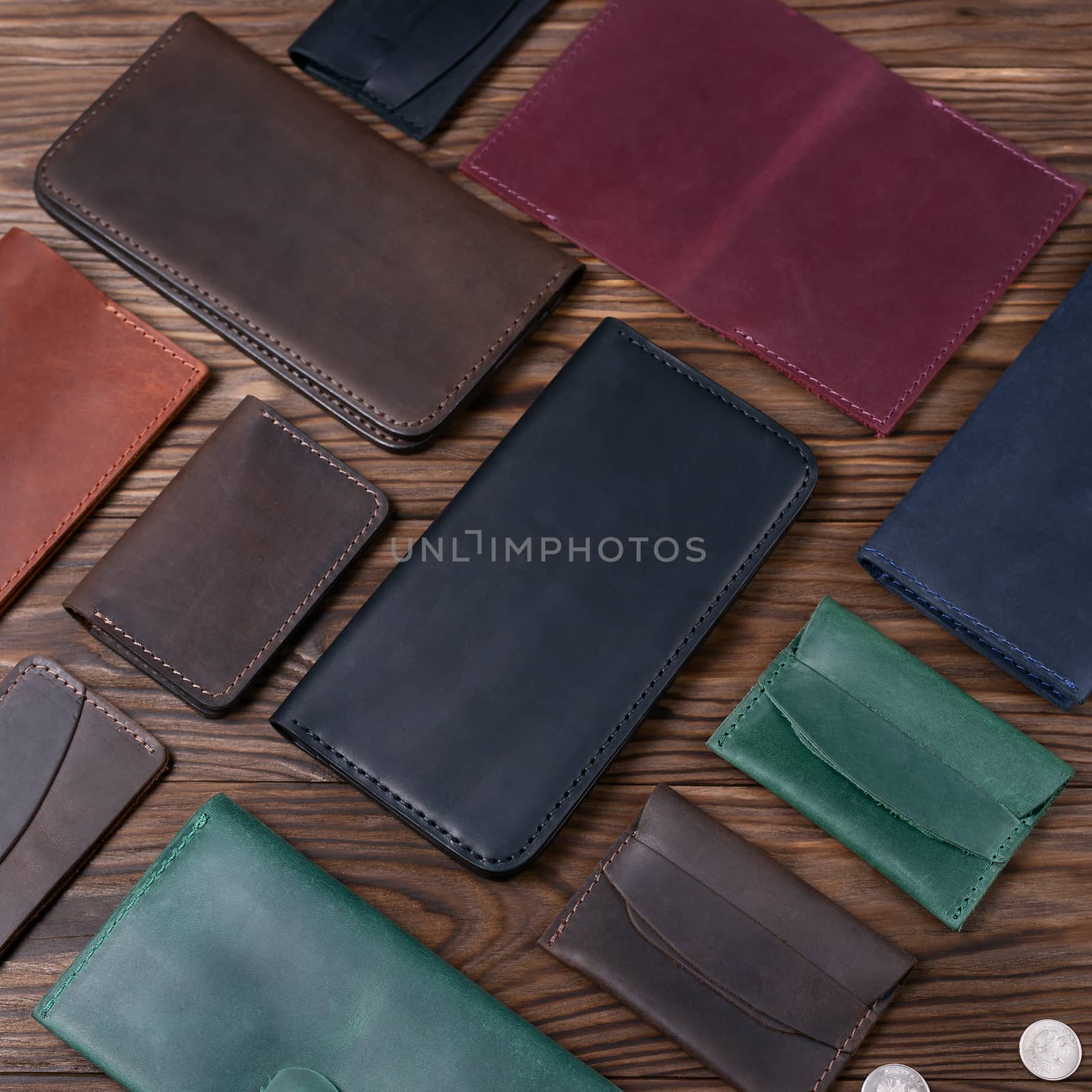 Black color handmade leather porte-monnaie surrounded by other leather accessories on wooden textured background. Side view. Stock photo of luxury accessories.