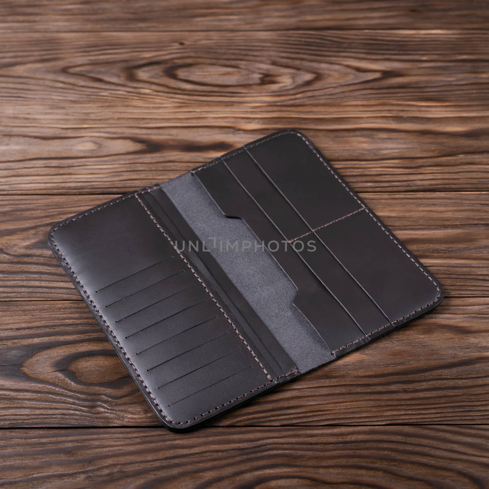 Dark blown gloss color handmade leather porte-monnaie on wooden textured background. Purse is opened and empty. Side view. Stock photo of luxury accessories.