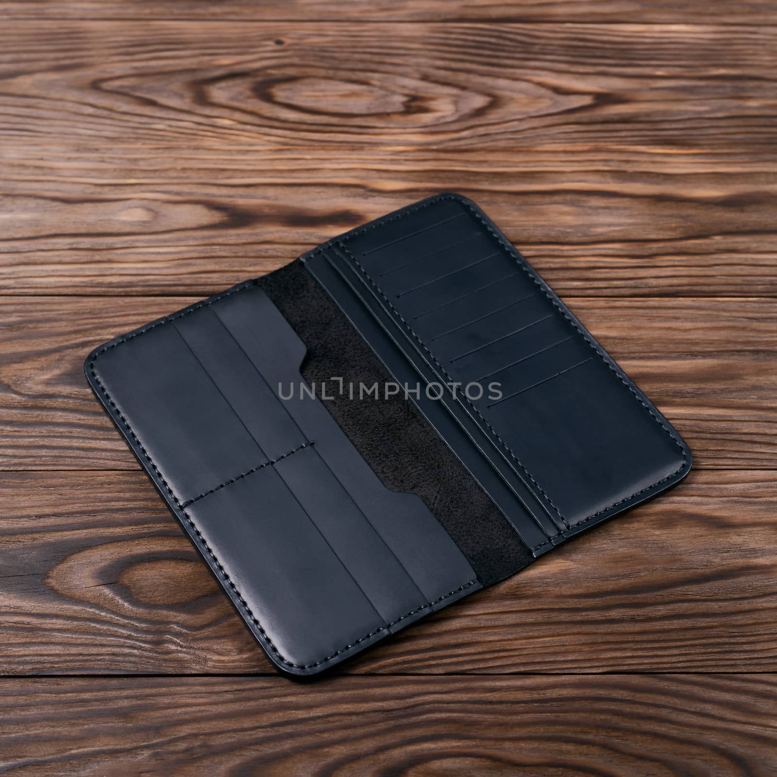 Black color handmade leather porte-monnaie on wooden textured background. Purse is opened and empty. Side view. Stock photo of luxury accessories.