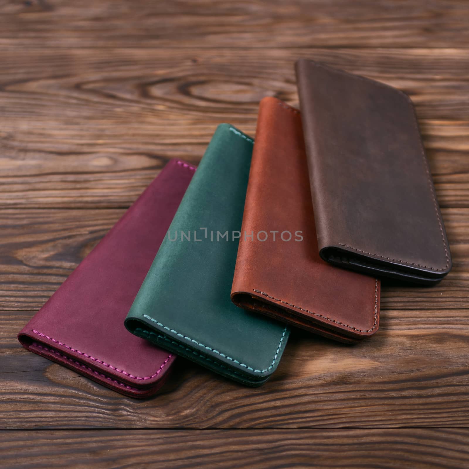 Four handmade leather porte-monnaie on wooden textured background. Side view. Stock photo of luxury accessories.