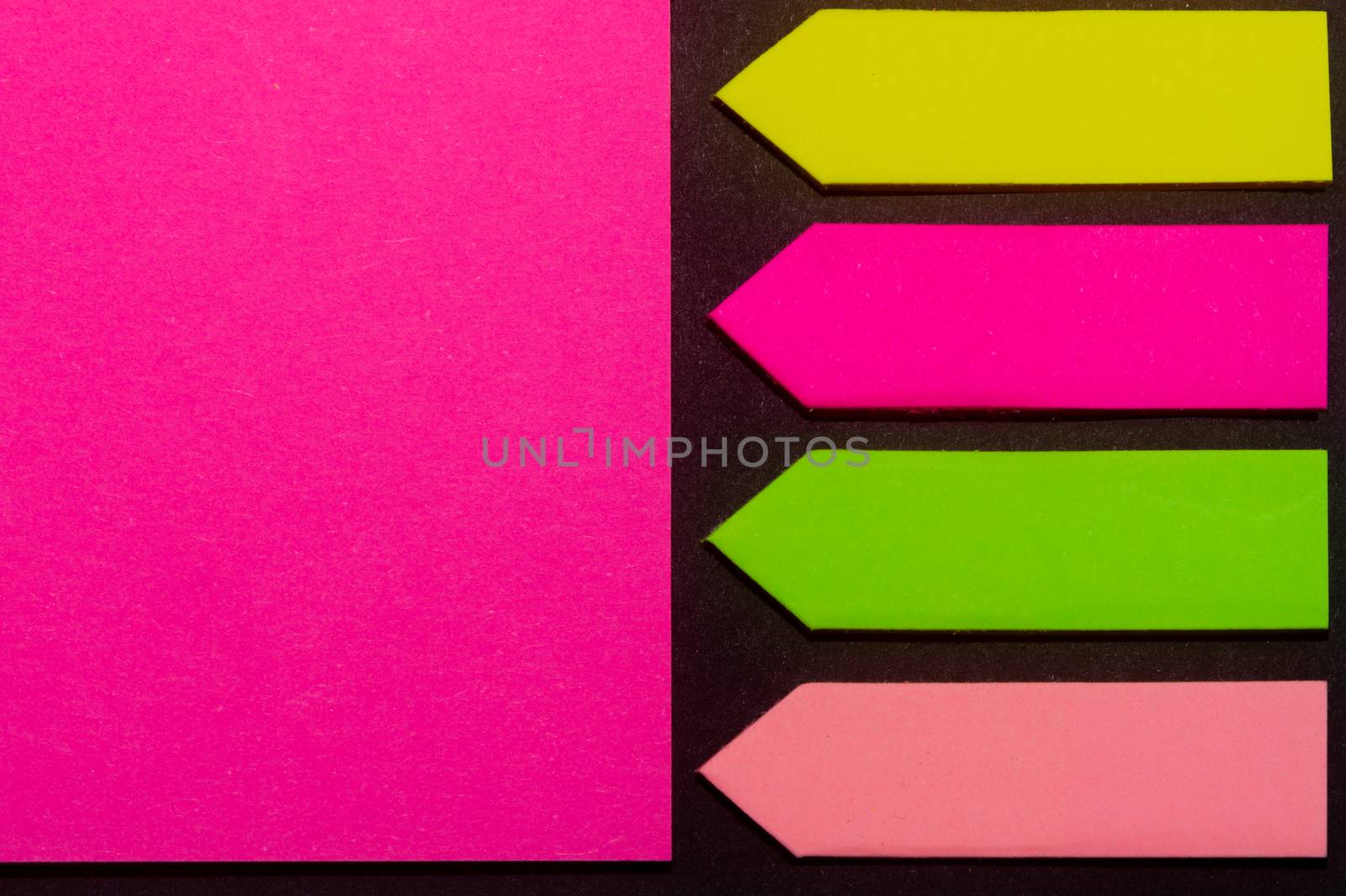 Green, yellow, purple and rose hue colorful office stickers on black paper. Office noteparer as reminder. Isolated on black paper.