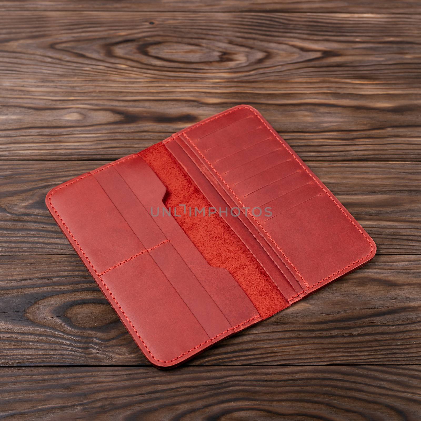 Hue red color handmade leather porte-monnaie on wooden textured background. Purse is opened and empty. Side view. Stock photo of luxury accessories.