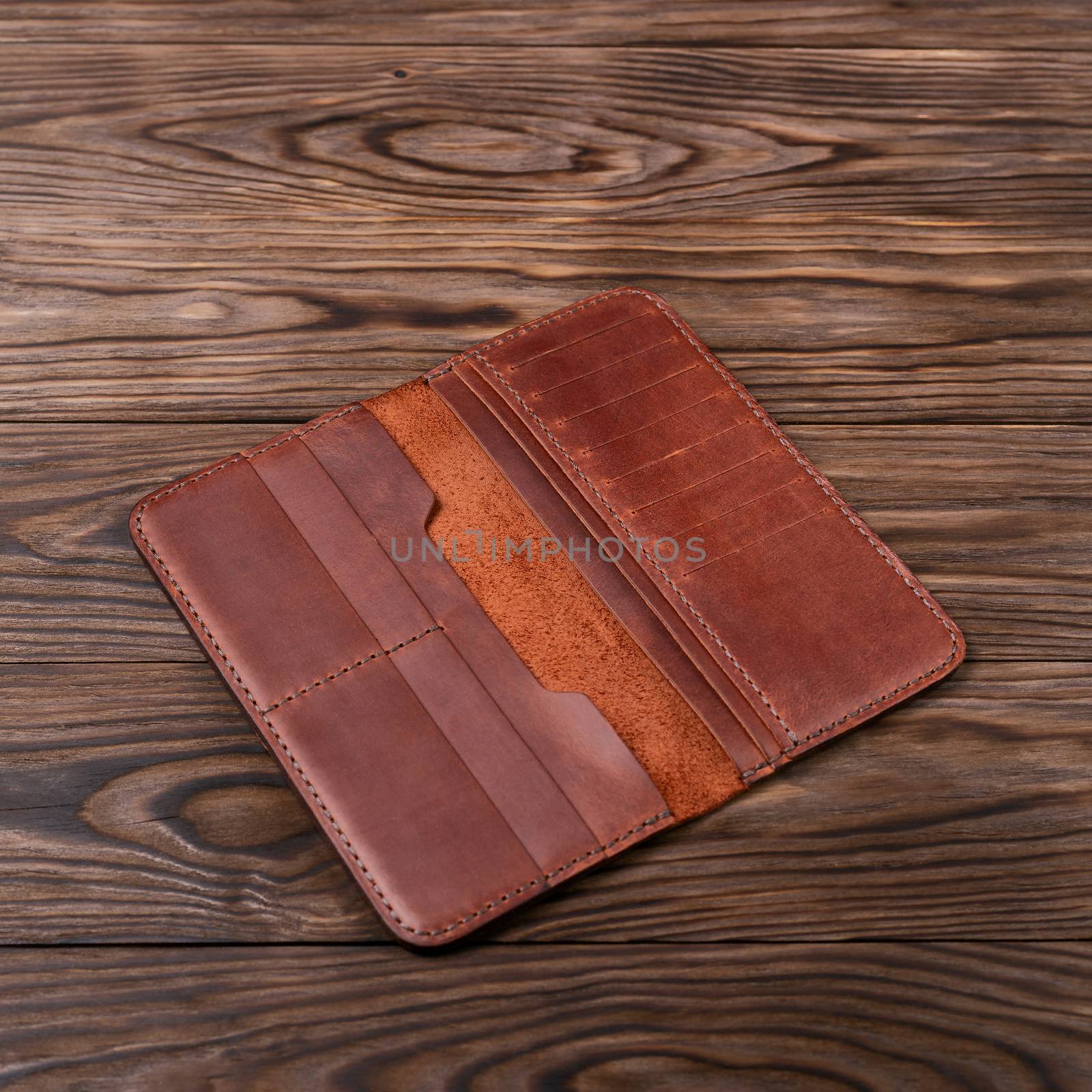 Red color handmade leather porte-monnaie on wooden textured background. Purse is opened and empty. Side view. Stock photo of luxury accessories.