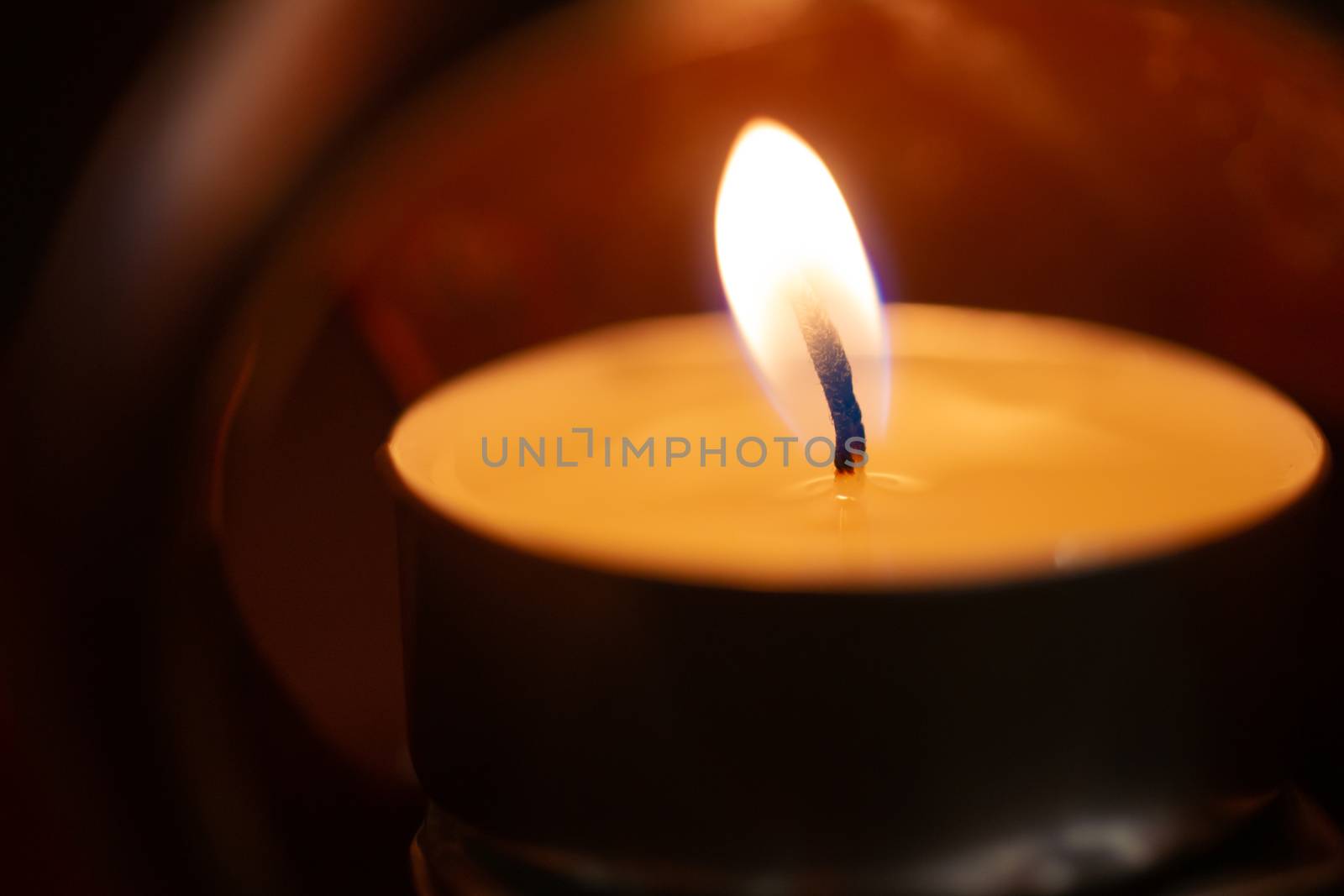 Underexposed low light photo of candle in aromatic lamp. Close-up view