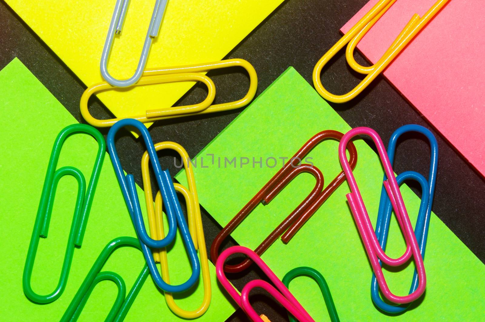 Paperclips on colorful different colour office stickers on black paper.