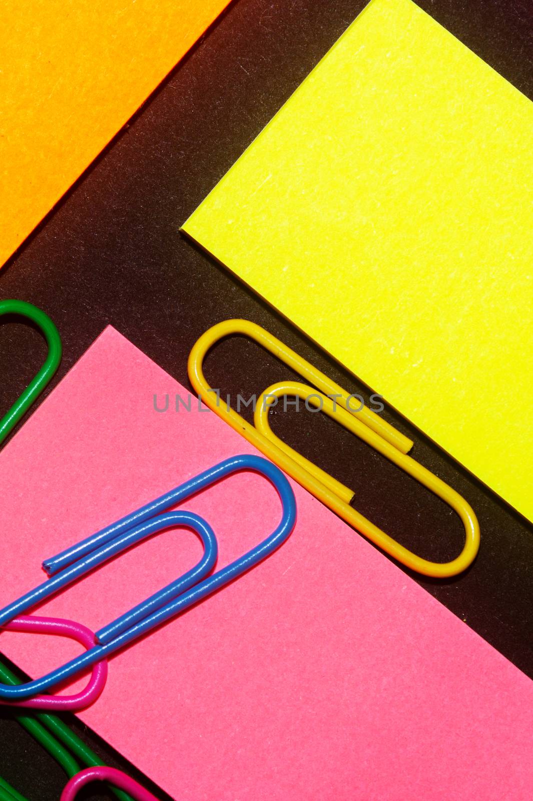Paperclips on colorful different colour office stickers on black paper.