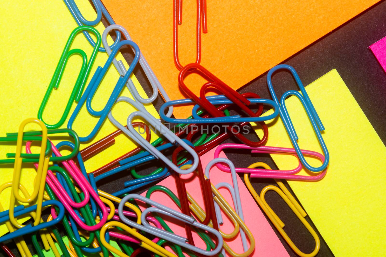 Paperclips on colorful different colour office stickers on black paper.