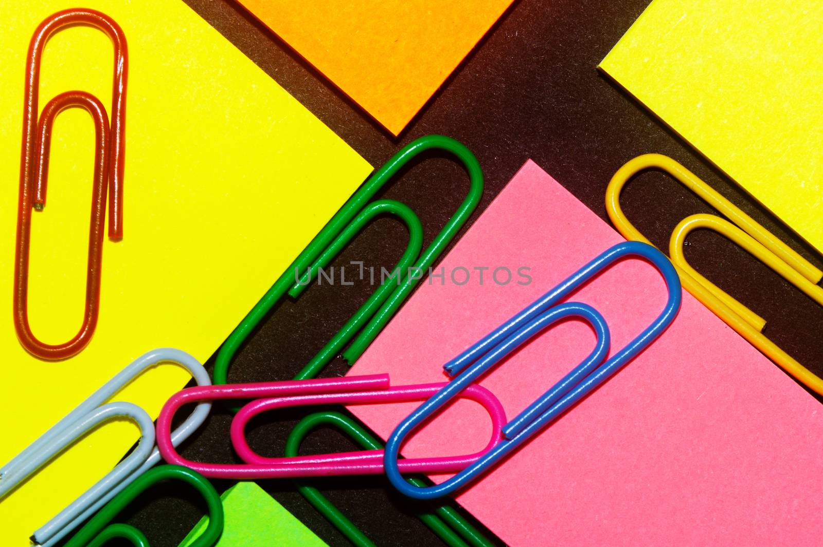 Paperclips on colorful different colour office stickers on black paper.