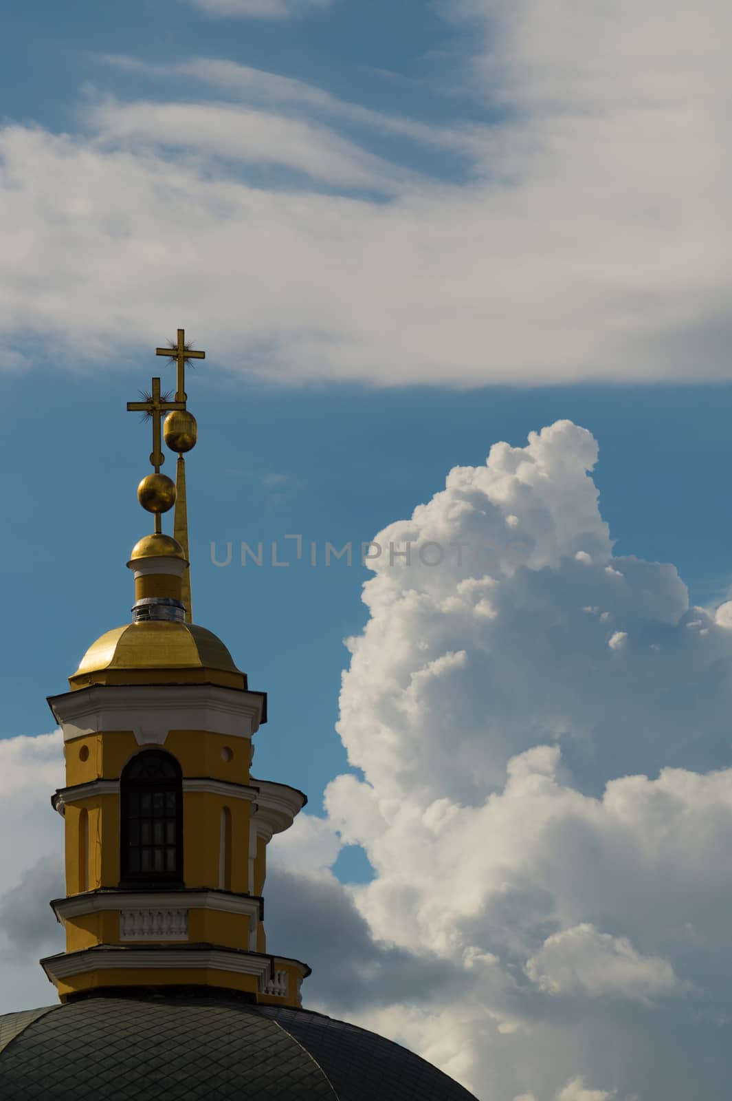 a yellow dome of a christian church against a blue sky with invasive clouds.