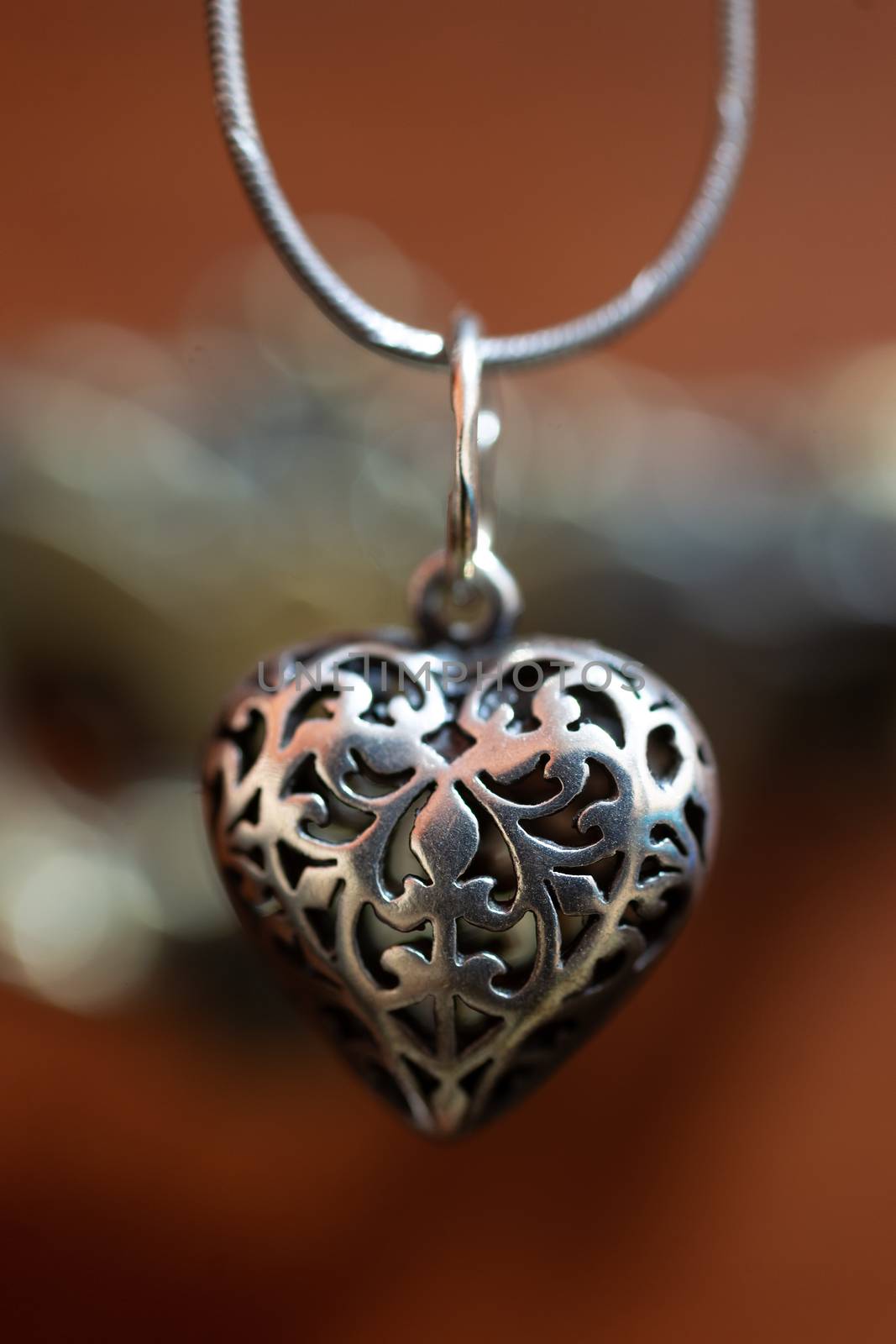 Close up photo of female neck silver pendand on blurred background. A handwork sterling silver pendant look as heart. Macrophoto with blurred background.