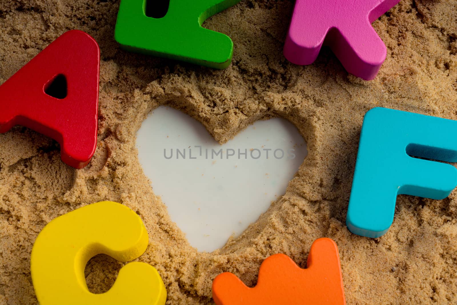 Heart shape and colorful Letters made of wood on sand