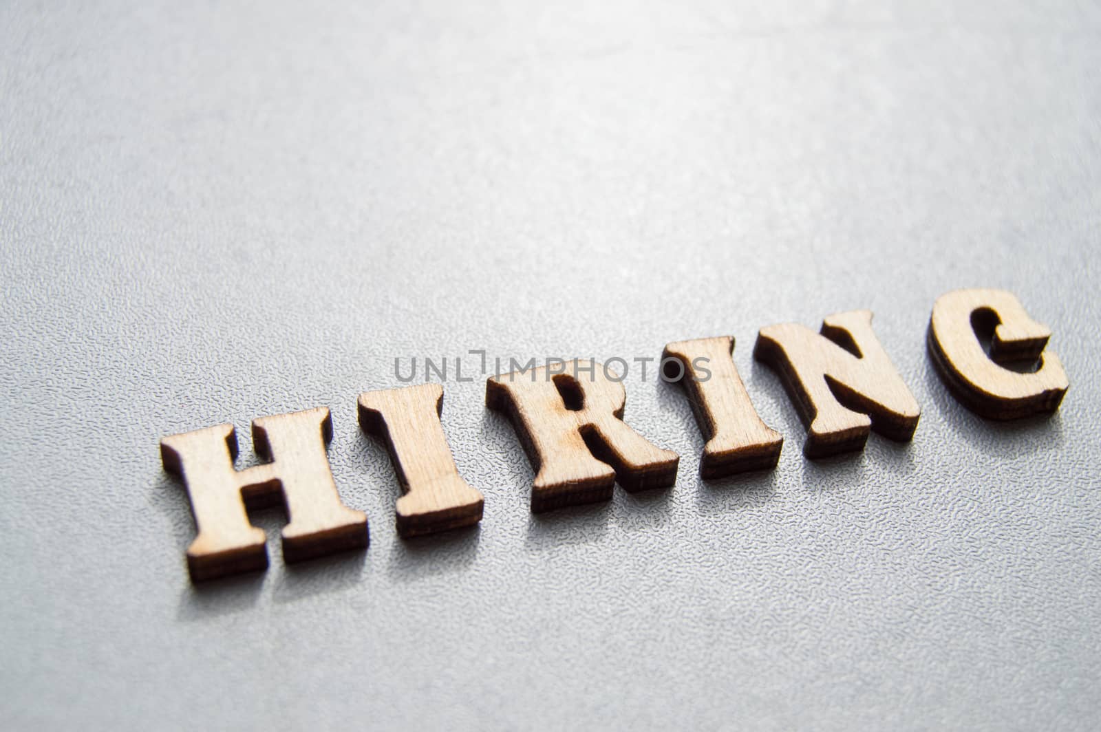 Advertising hiring is represented by the word HIRING, made of wooden letters on a gray background. Ready-made layout for the designer with space for text and copy space