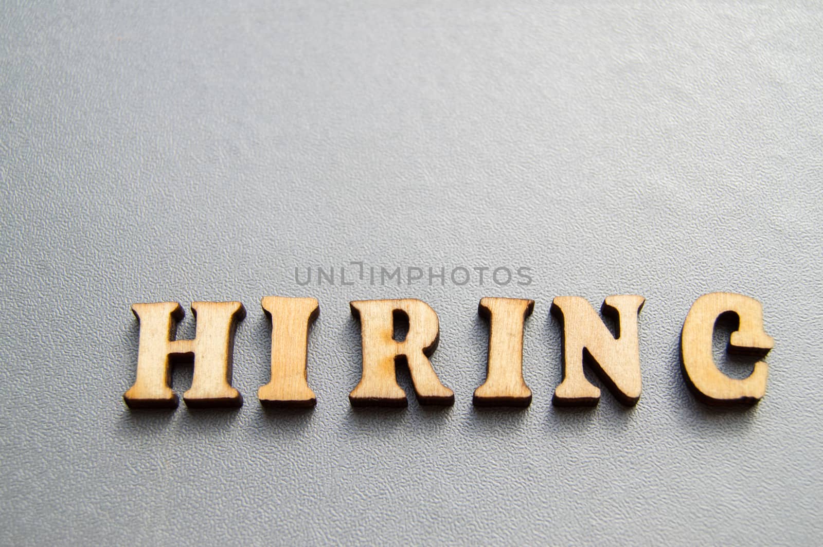 Advertising hiring is represented by the word HIRING, made of wooden letters on a gray background. Ready-made layout for the designer with space for text and copy space