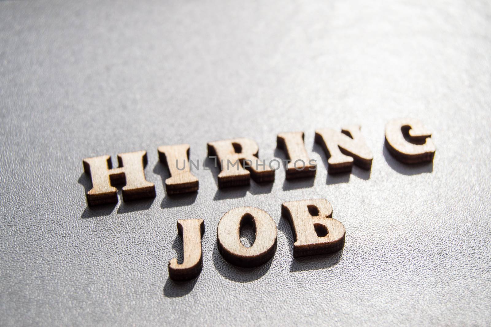 The concept of hiring workers, written by HIRING JOB in wooden letters on a gray background with selective focus and space for your by claire_lucia
