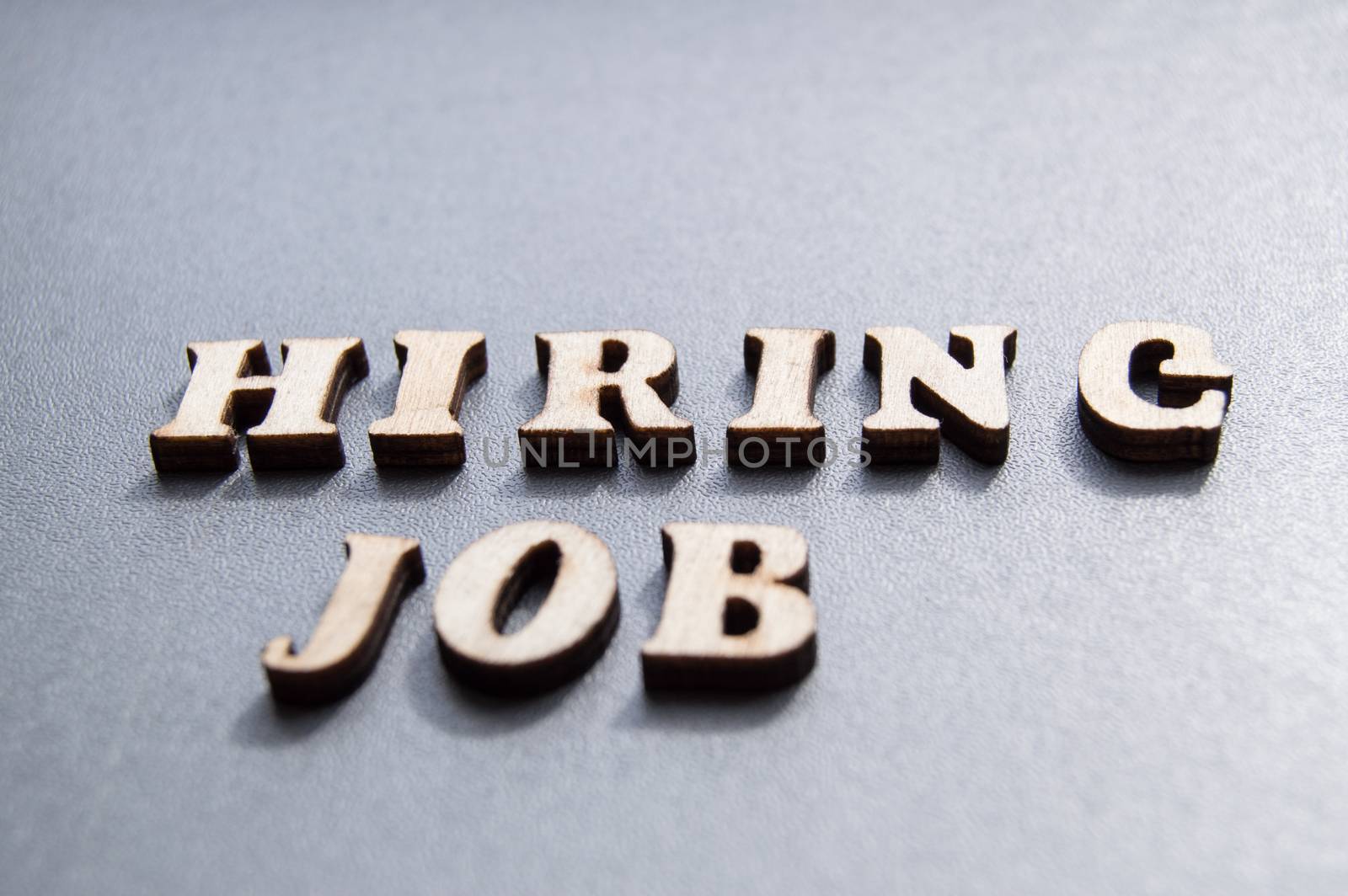 The concept of hiring workers, written by HIRING JOB in wooden letters on a gray background with selective focus and space for your by claire_lucia