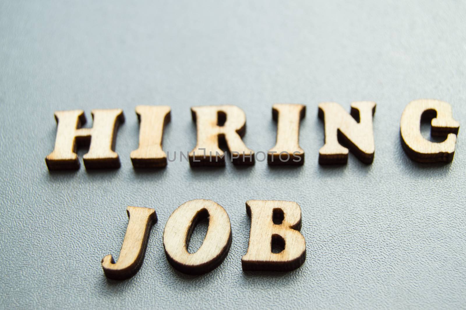 The concept of hiring workers, written by HIRING JOB in wooden letters on a gray background with selective focus and space for your by claire_lucia