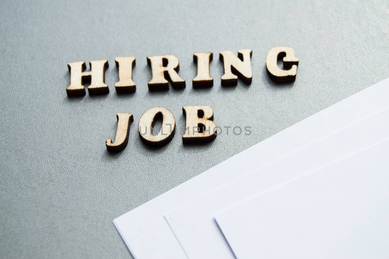 Hiring JOB is written in wooden letters on a gray background, near white sheets of paper, layout for design, ad layout, hiring concept.