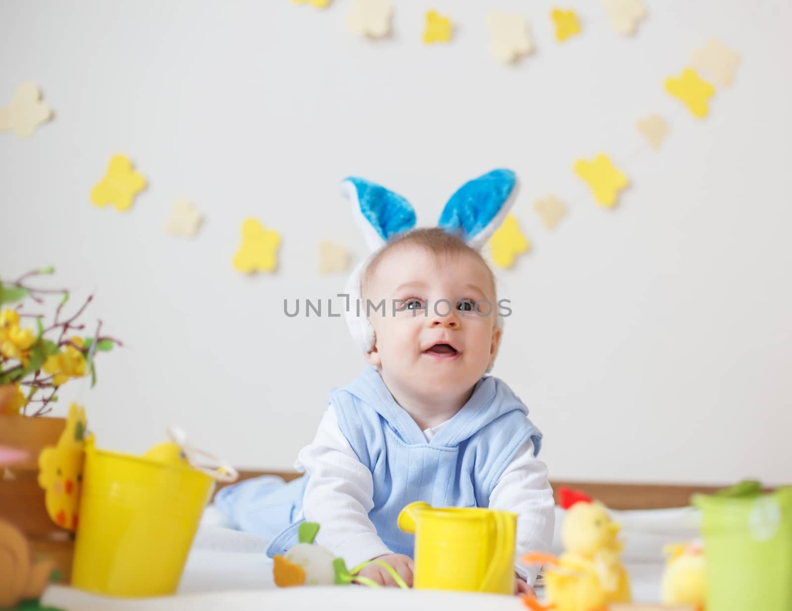 Cute baby boy with Easter bunny ears and colorful  flowers looking up