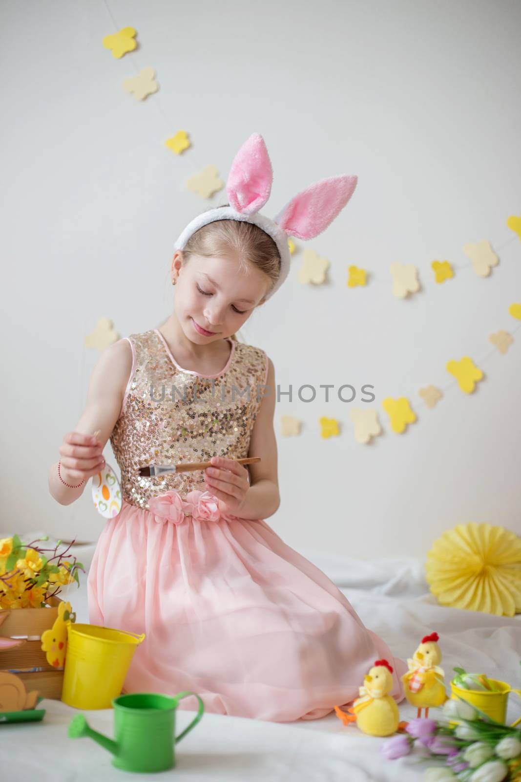 Cute little girl with bunny ears painting eggs, Easter decoration