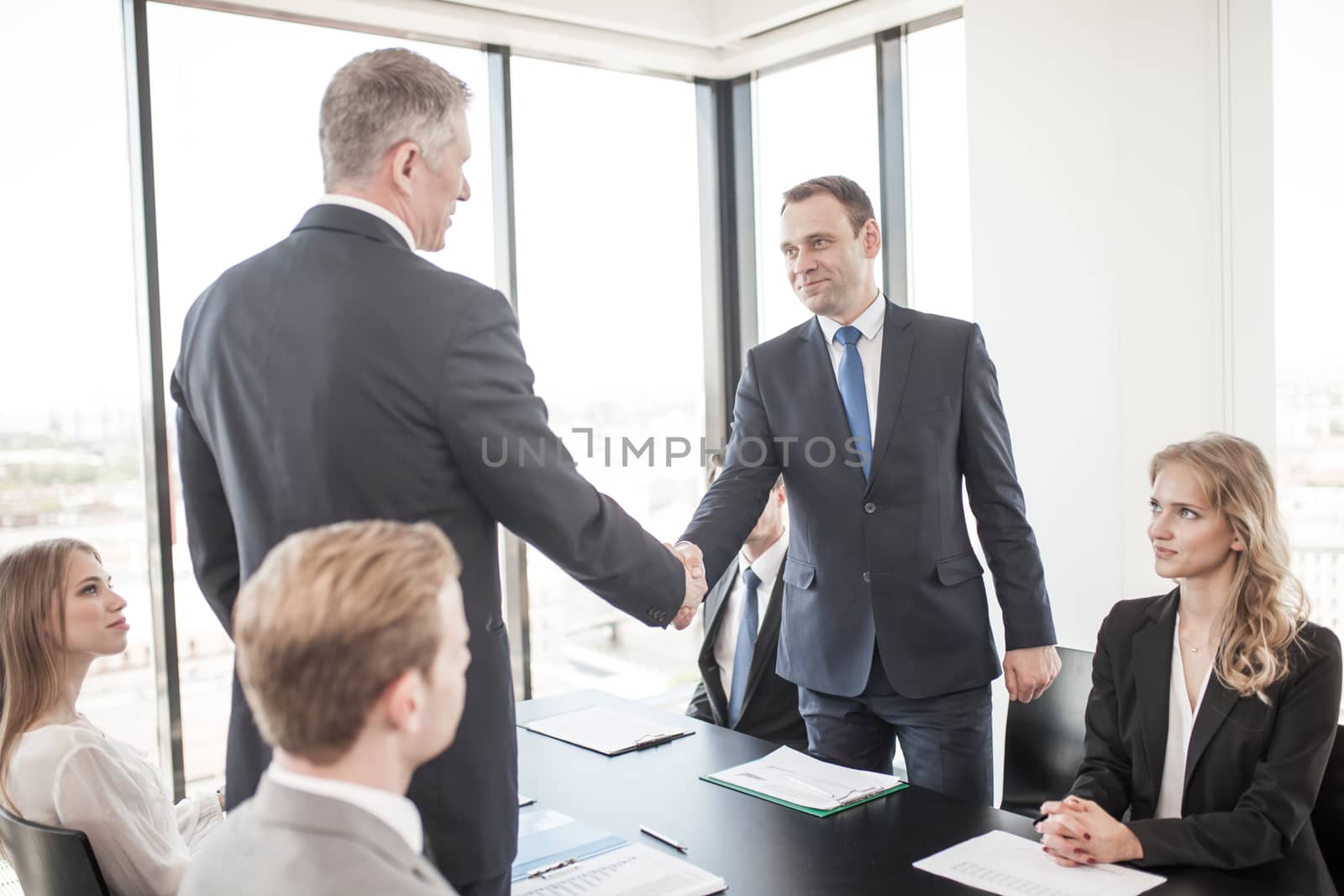 Handshake of business people at meeting in ofice , team sitting around table and discussing documents