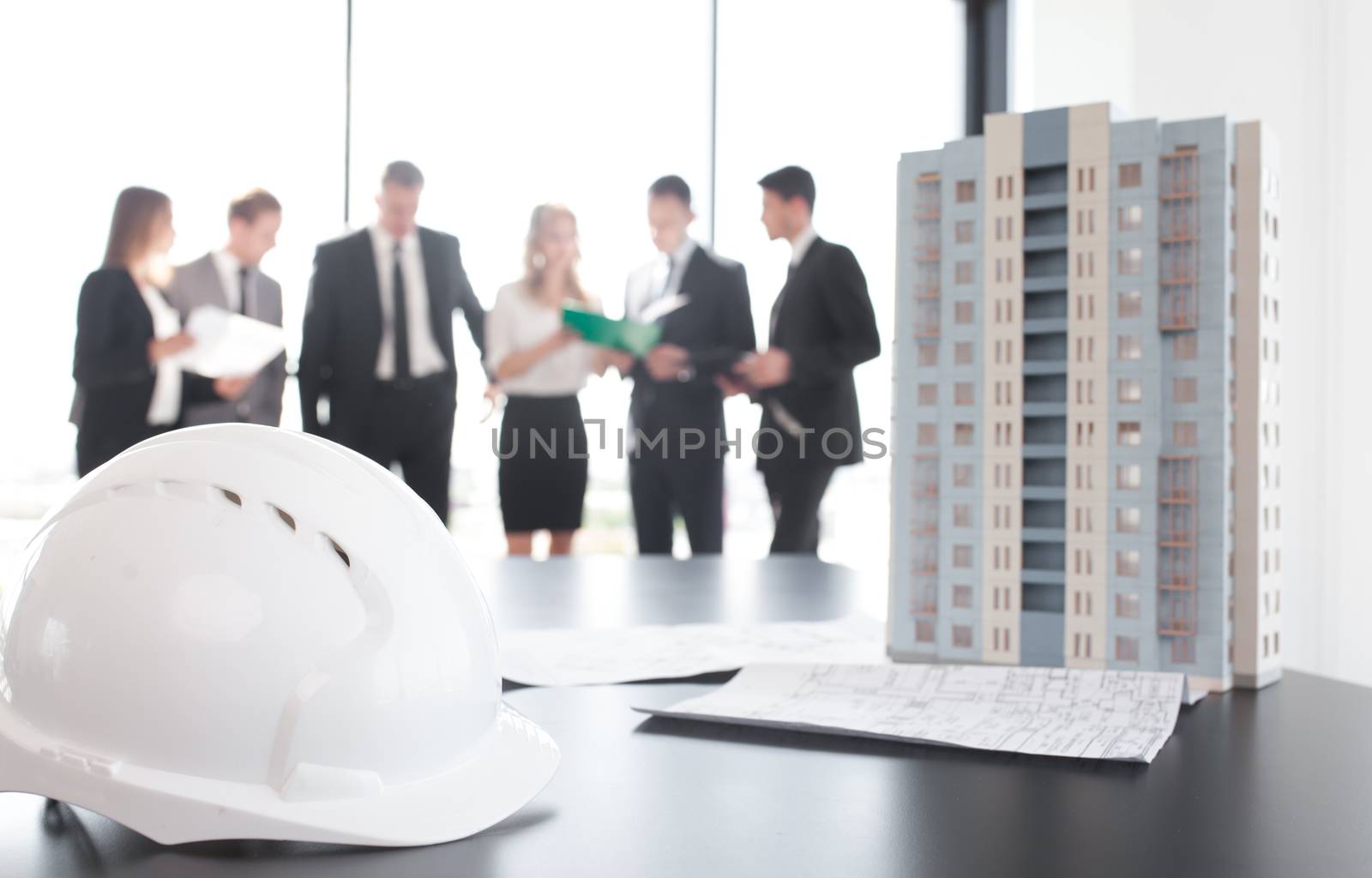 Business meeting of architects and investors, model of modern multi storey residential building house and hardhat on table , construction planning concept