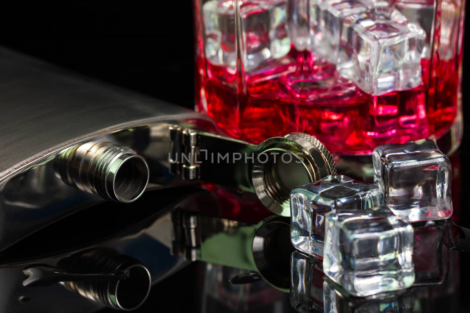 Stainless steel flask liquor alcohol and ice on table with red whiskey in glass on darkness background. Copy space for text or articles.