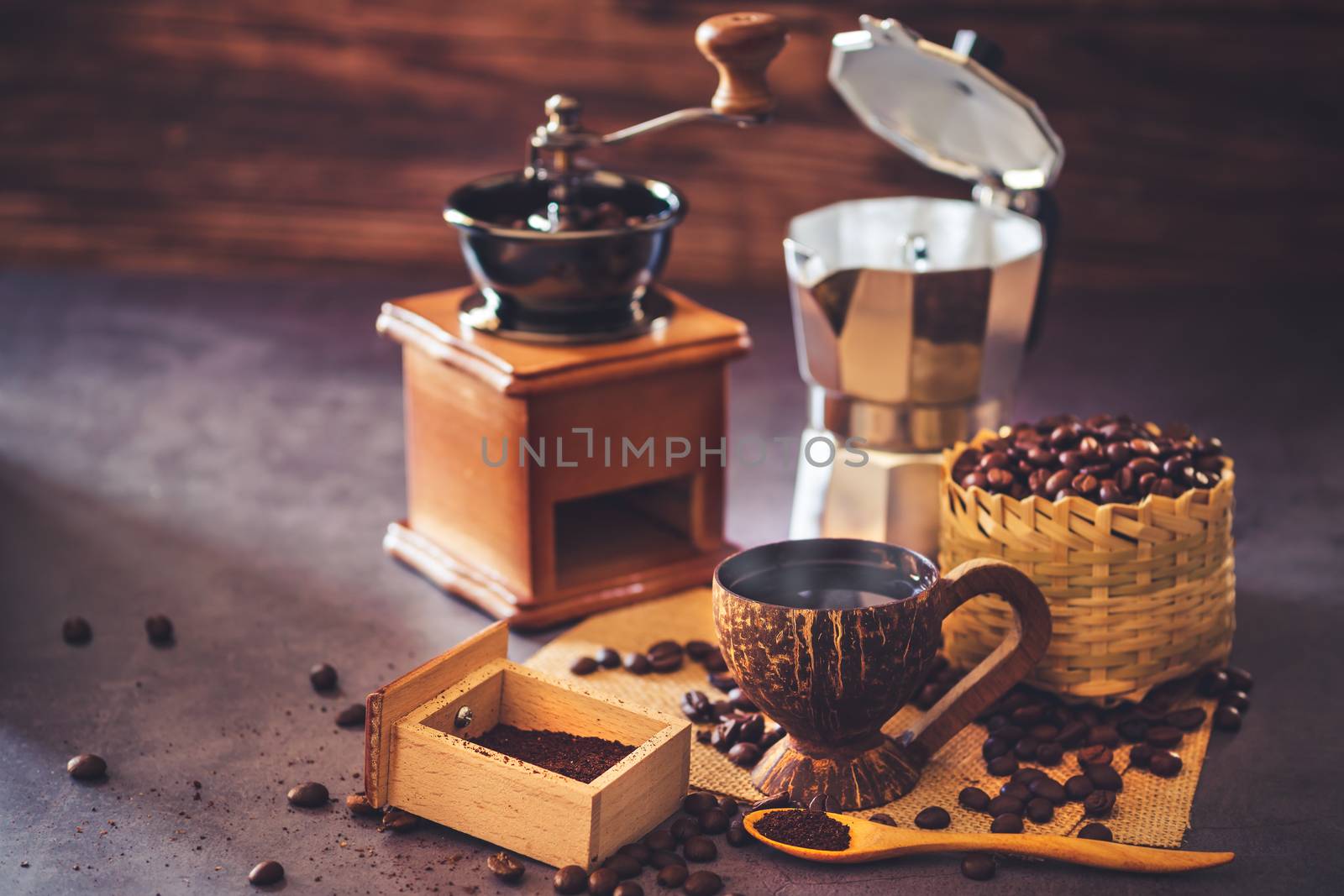 Brew black coffee in coconut cup and morning lighting. Roasted coffee beans in a bamboo basket and wooden spoon. Vintage coffee grinder and moka pot. Concept of coffee time in morning or start the new day.