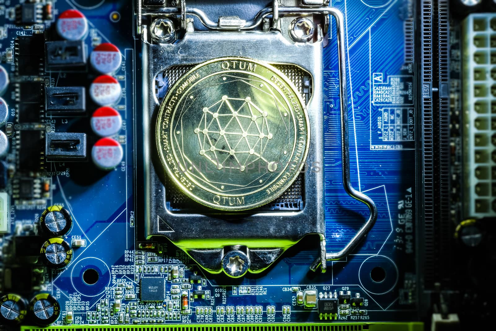 Top view of golden qtum cryptocurrency physical coin on computer mother board processor.Bitcoin mining farm, working computer equipment concept.