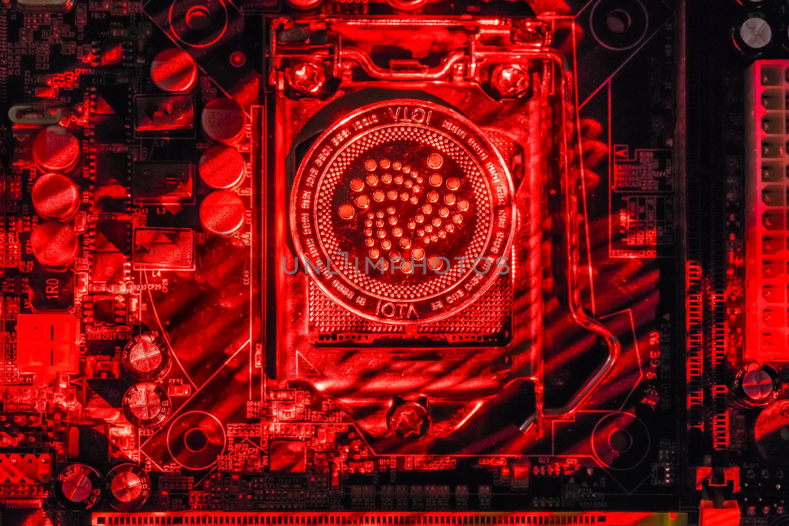 Top view of Iota cryptocurrency physical coin painted with laser light on computer mother board processor.Bitcoin mining farm, working computer equipment concept.