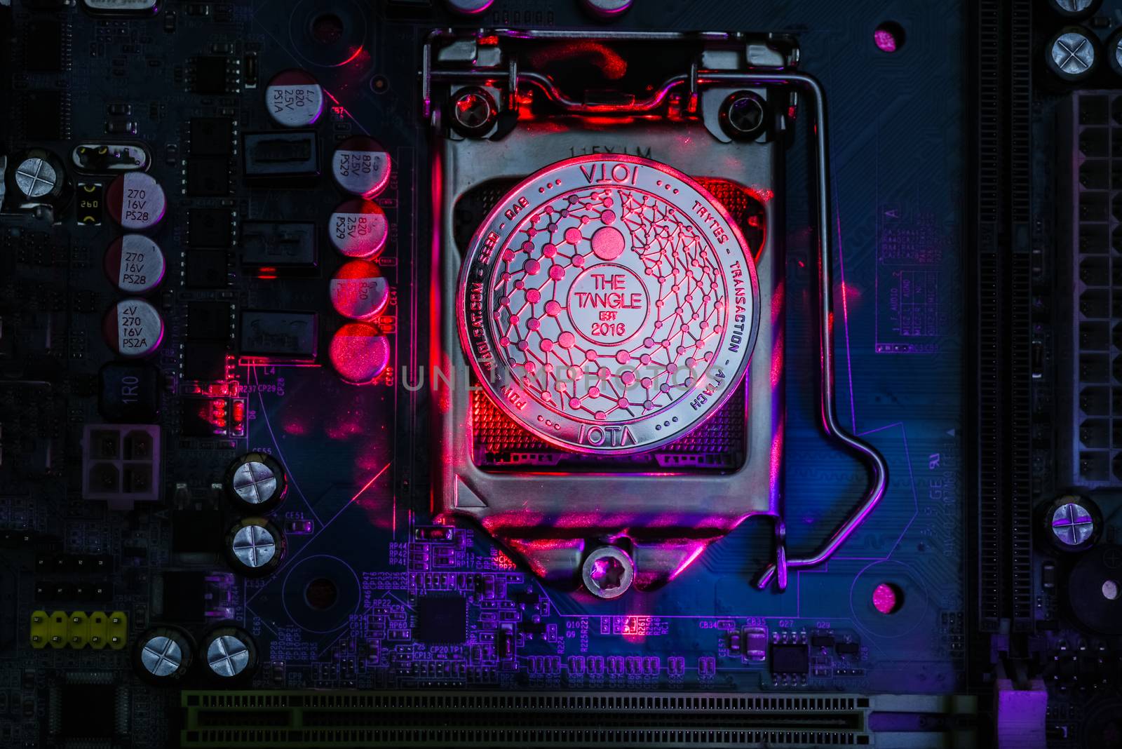 Top view of Iota cryptocurrency physical coin painted with laser light on computer mother board processor.Bitcoin mining farm, working computer equipment concept.