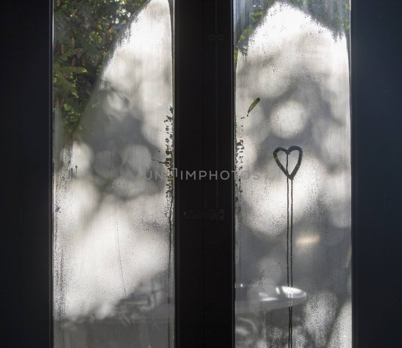Window dew and drawn heart shape with running drops