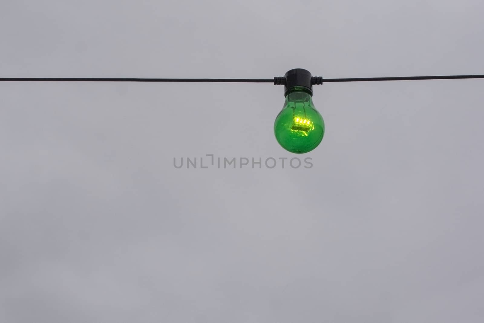 Green color lightbulb on string against gray sky background
