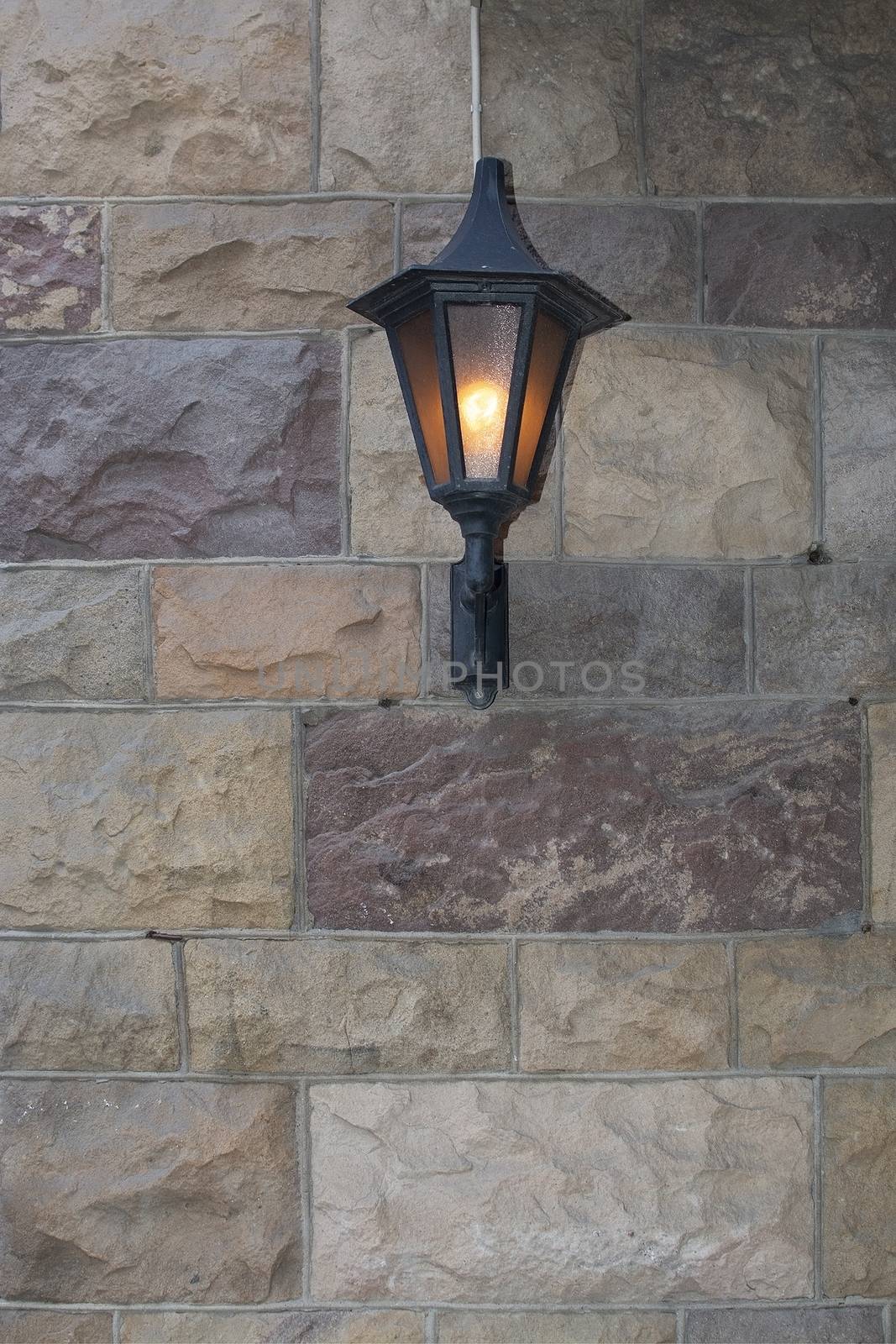 Wrought iron wall lamp on sandstone facade background copy space rustic texture.