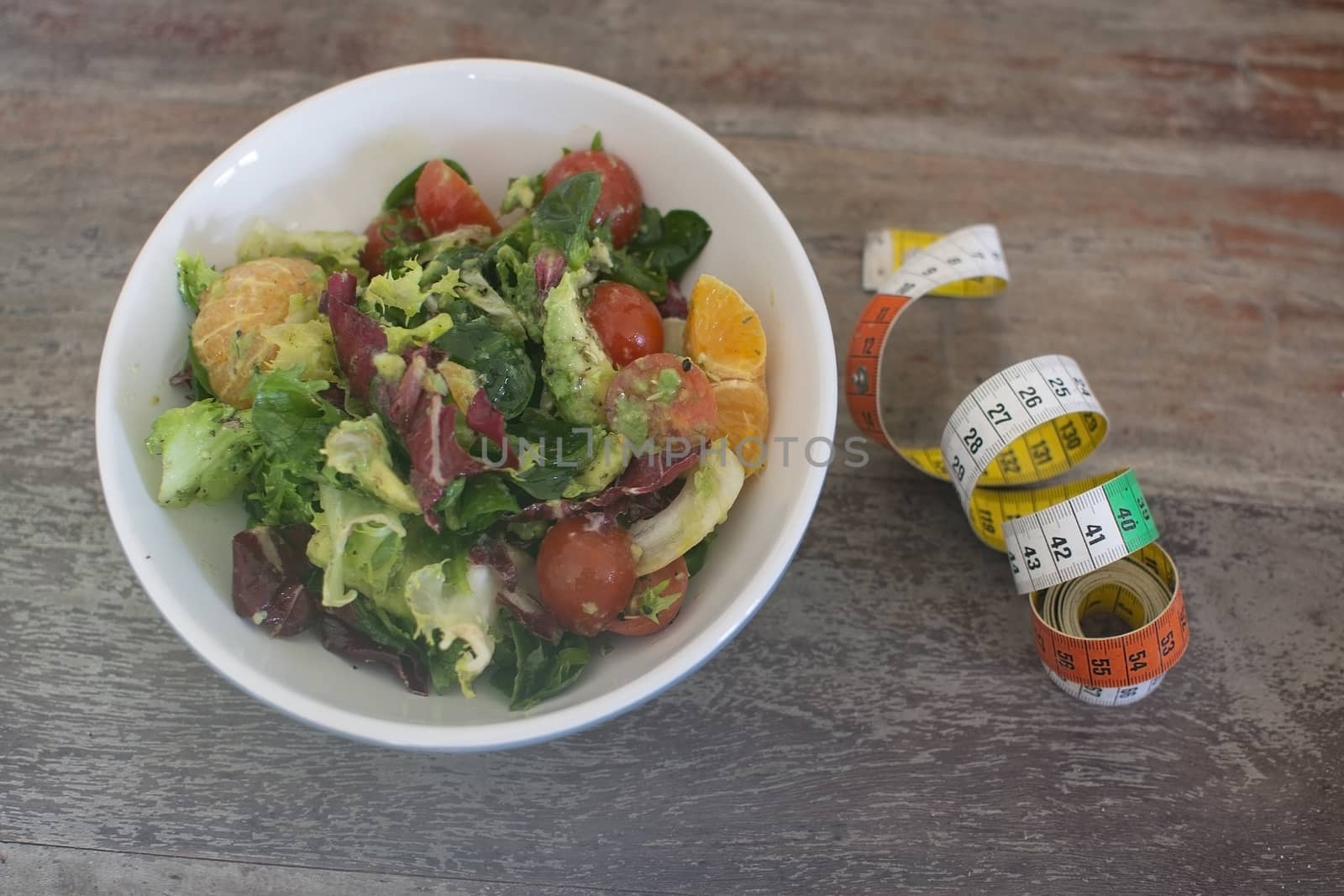 Mixed green and purple salad with measuring tape on shabby brown wooden table dieting fitness health conceptual background.