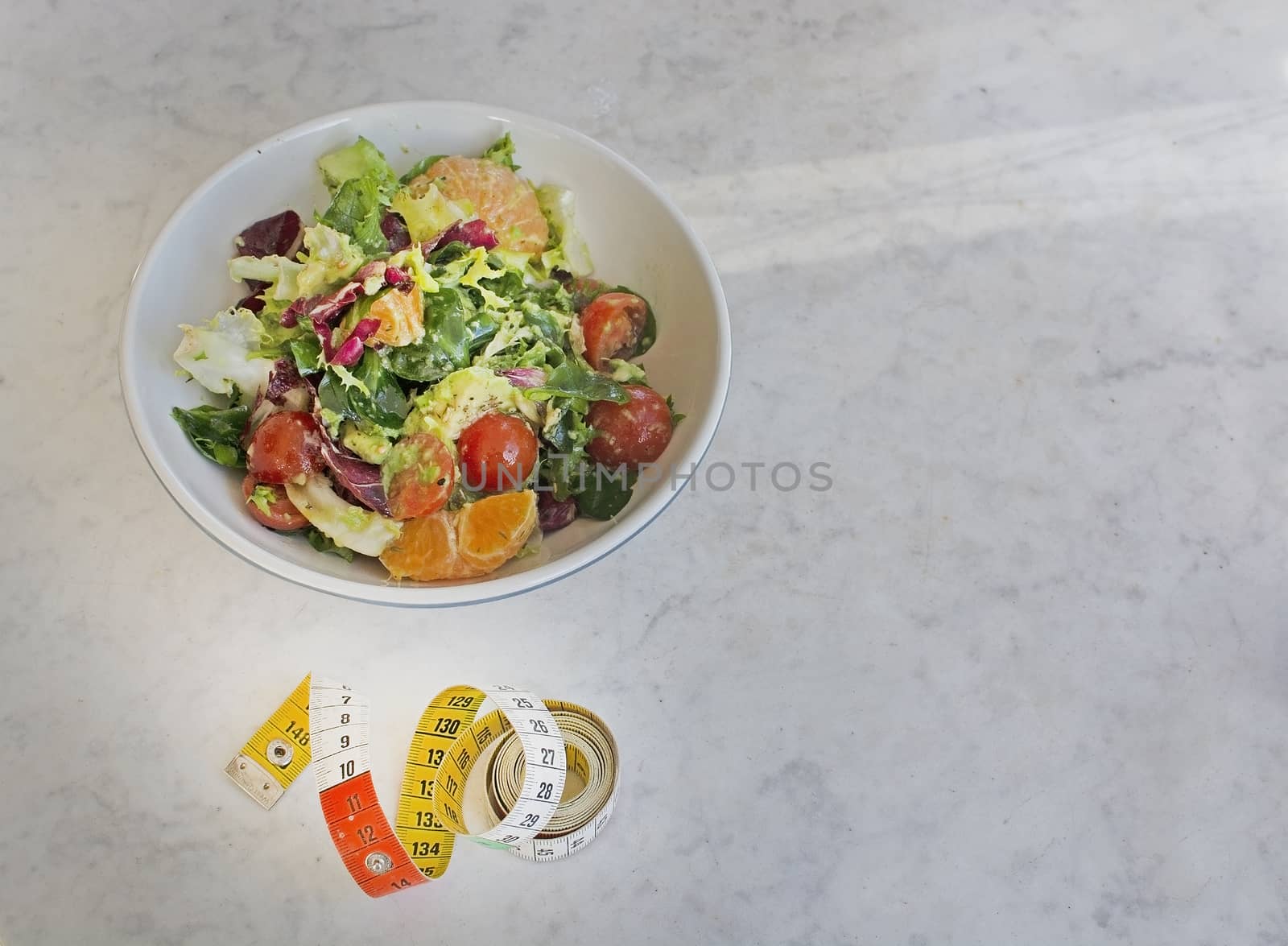 Mixed green and purple salad with measuring tape on white marble table dieting fitness health conceptual background with shadow for copy space