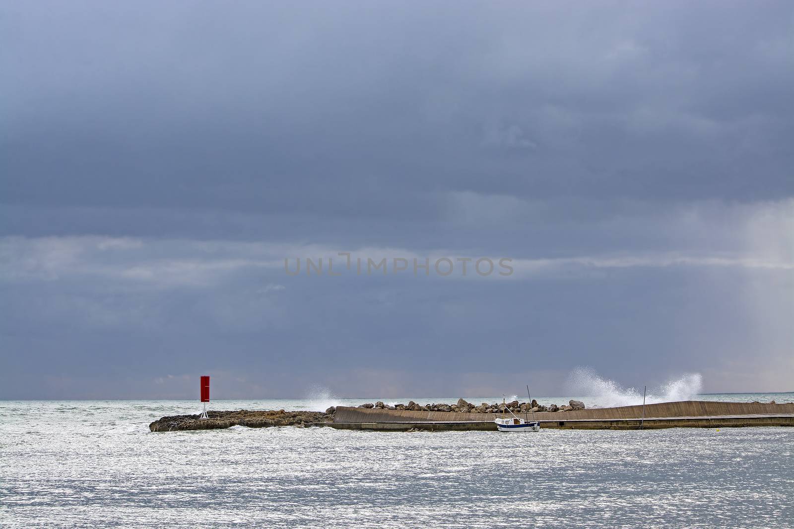 Mediterranean sea view with pier against dark skies with dramatic light on splashing wave on a winter day in Mallorca, Spain.