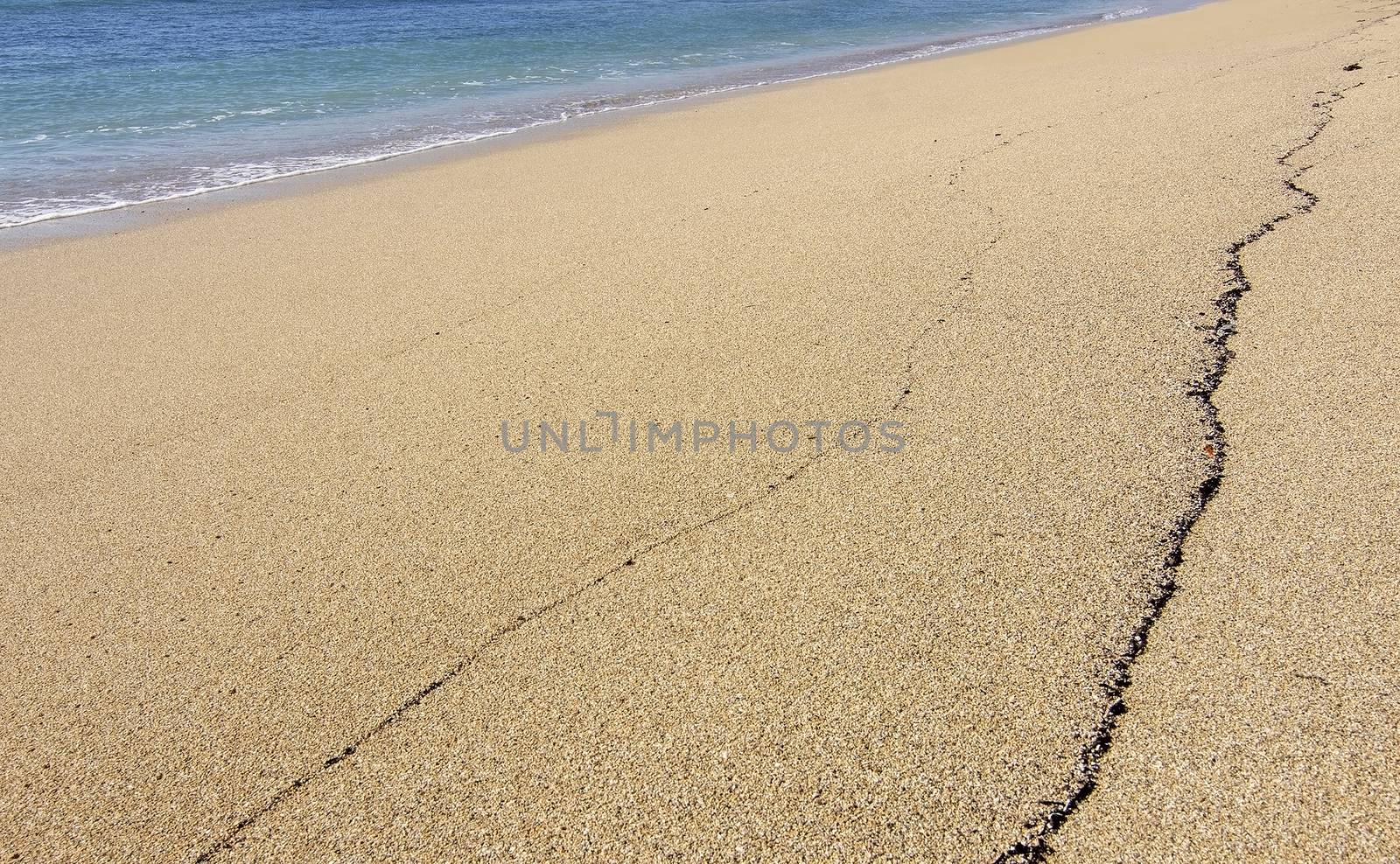 Untouched sand beach with wave residue pattern and blue sea in Mallorca, Spain.