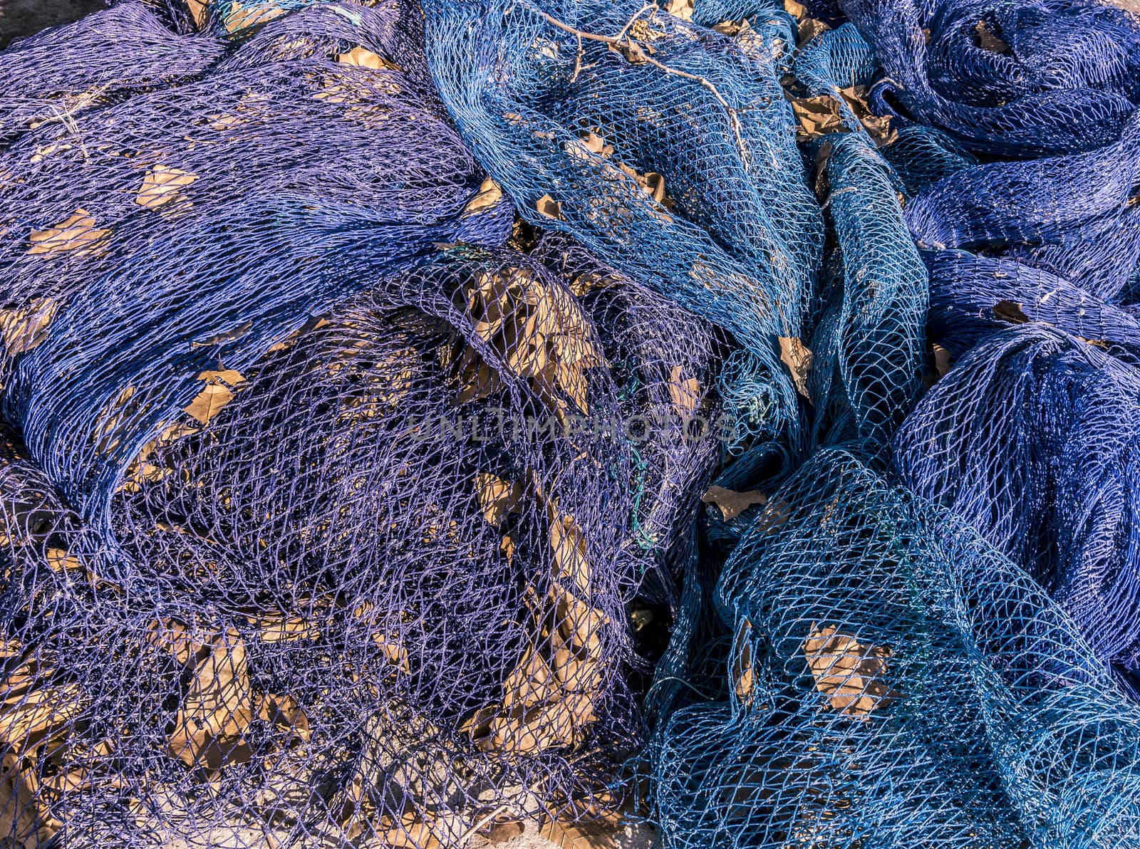 Blue fishing nets in a heap with old autumn leaves on a sunny winter day in Mallorca, Spain.