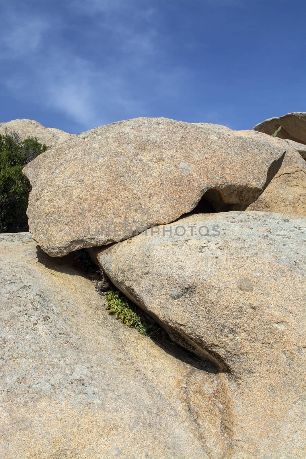 Slab of granite rock lying on top of eroded cliff with blue sky wispy cloud in Costa Smeralda, Sardinia, Italy.