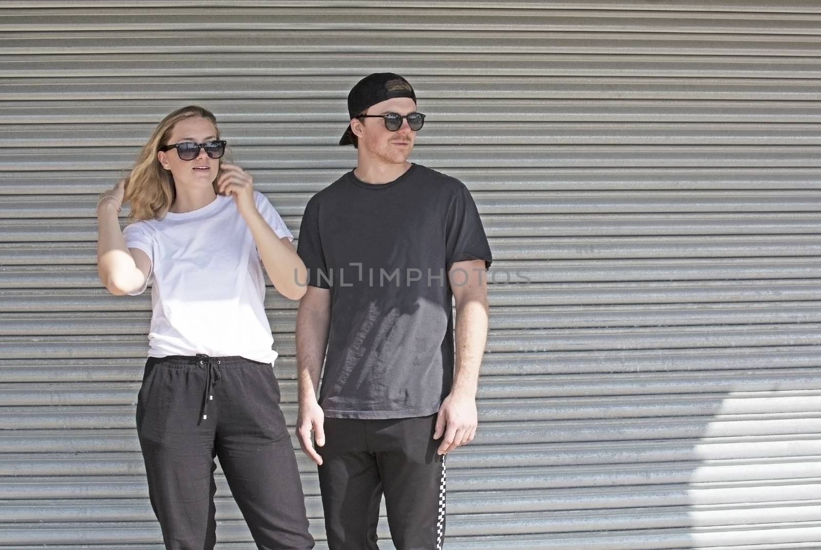 Young natural and casual sporty couple dressed man with cap backwards and woman against corrugated iron wall street style