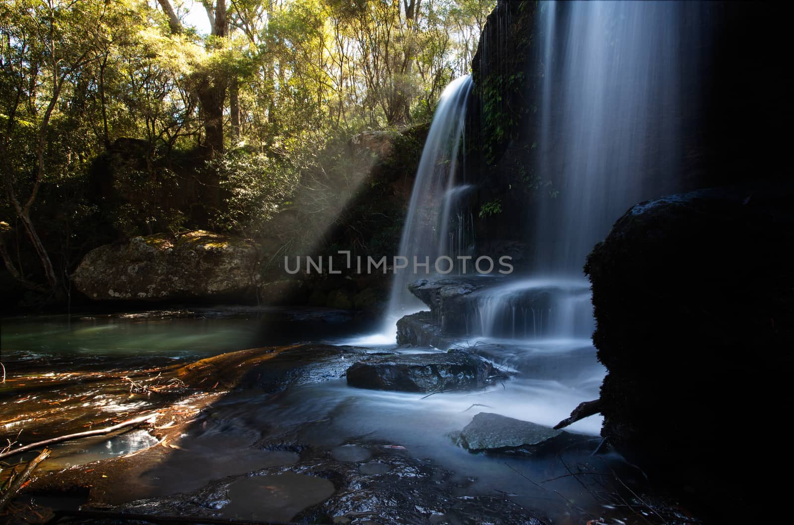 Sunlight streaming through trees of the surrounding bushland of a beautiful waterfall and swimming hole in Southern Highlands