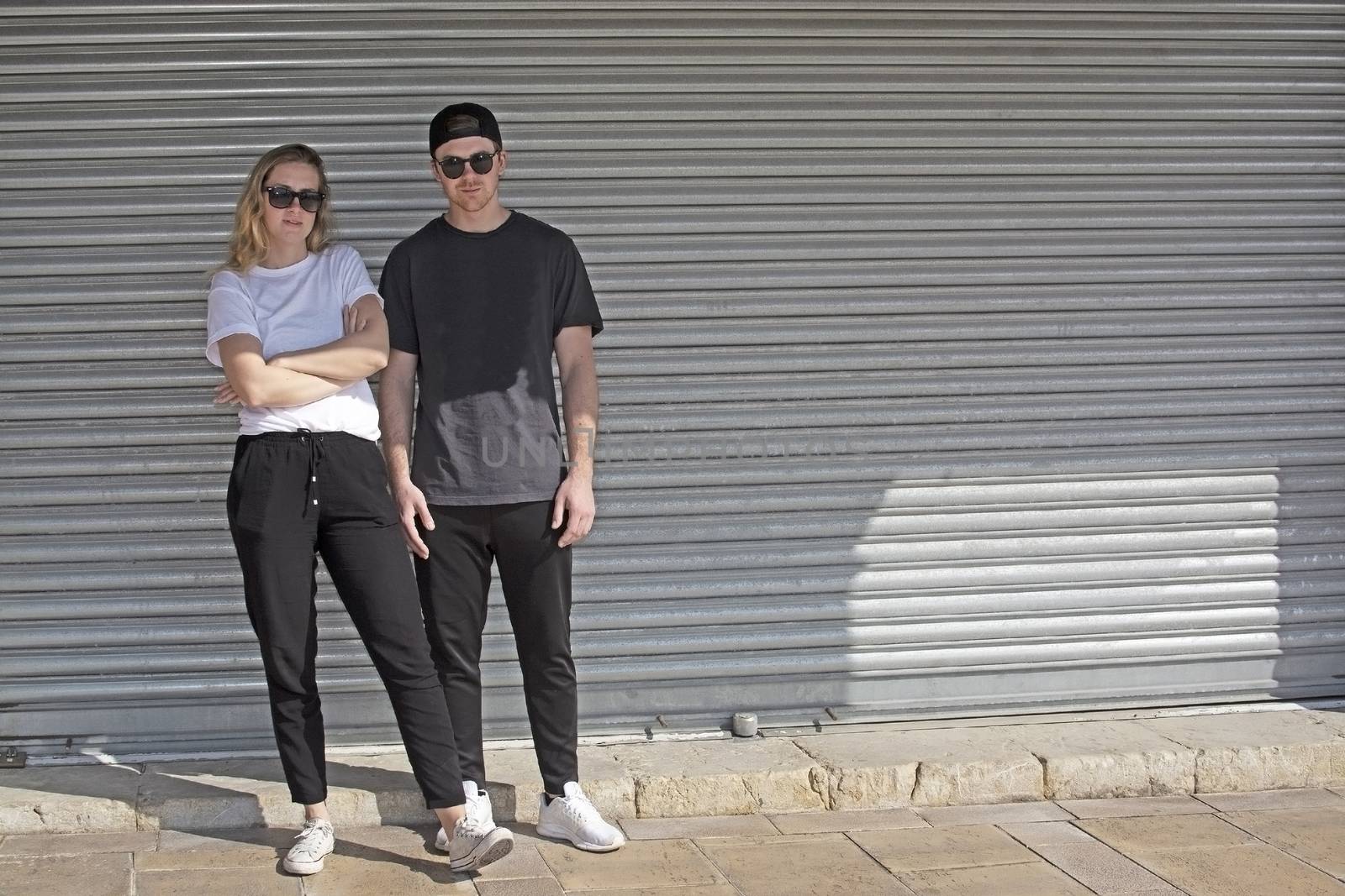 Young natural and casual sporty couple dressed man with cap backwards and woman against corrugated iron wall street style