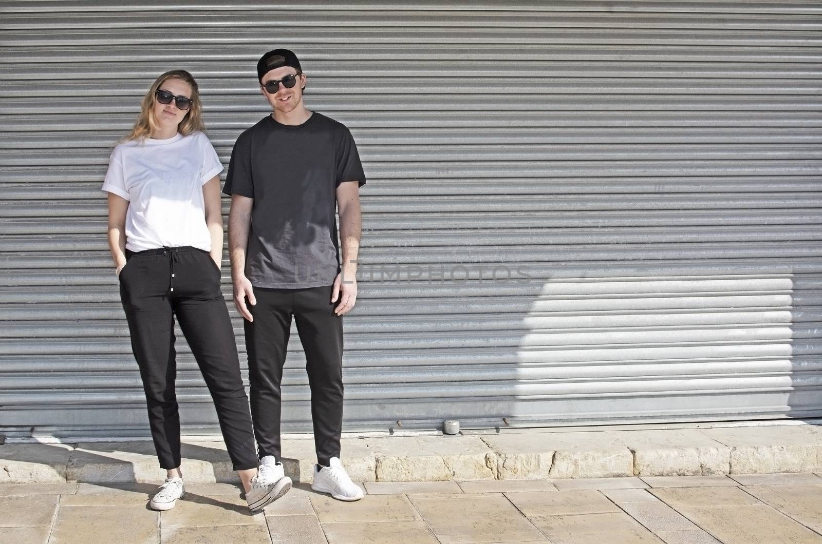 Young natural and casual sporty couple dressed man with cap backwards and woman against corrugated iron wall street style