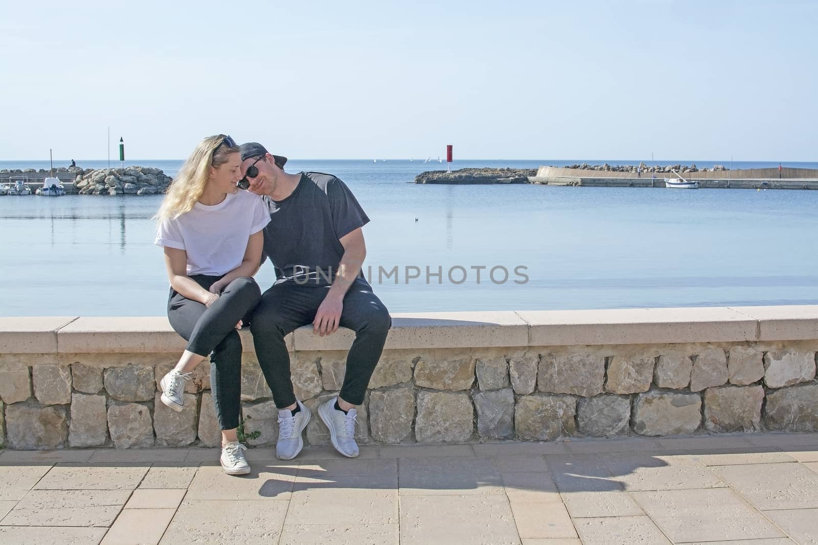 Young natural smiling and casual sporty couple sit on stone wall by ArtesiaWells
