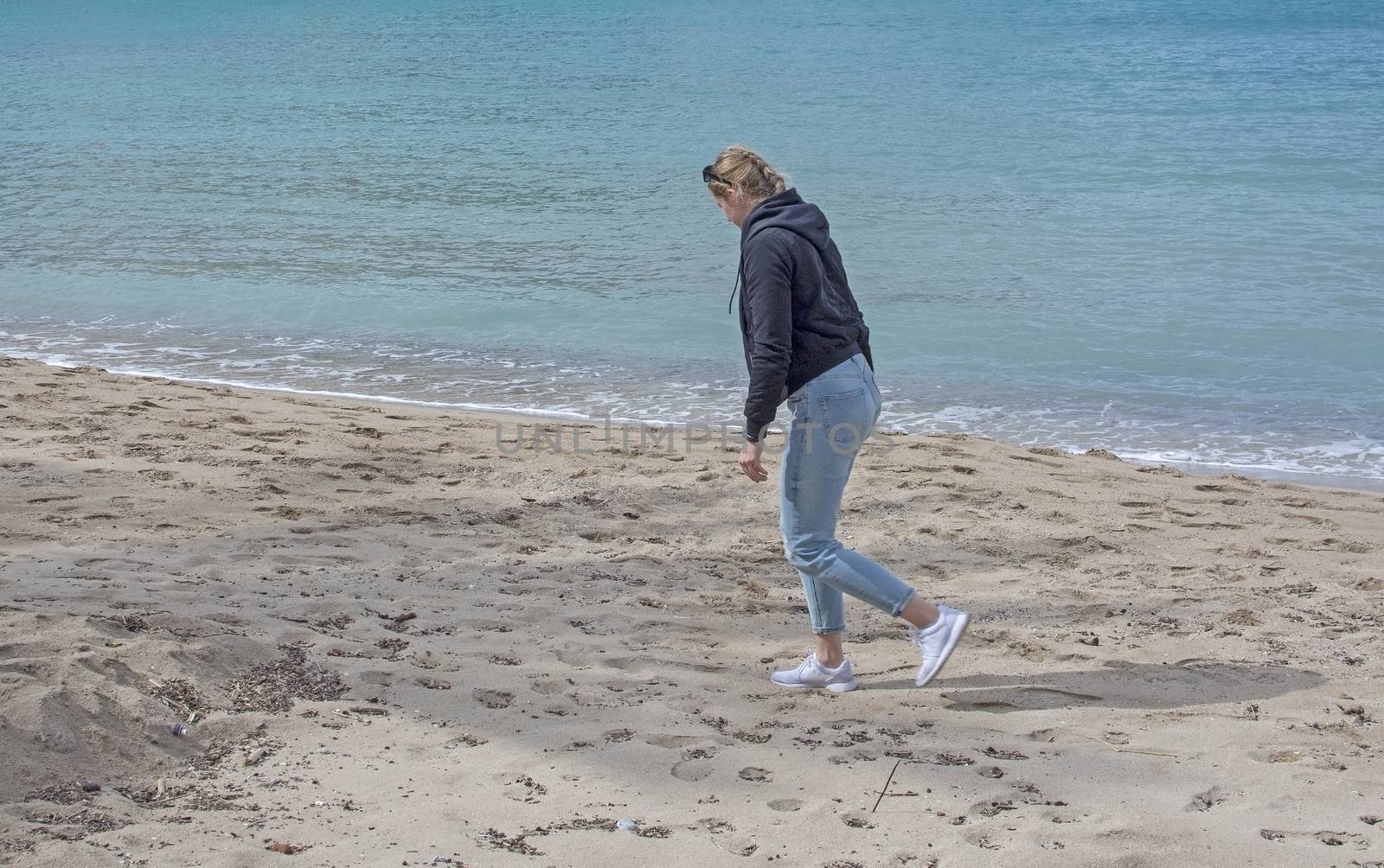 Young cute woman walks on sandy beach in spring near turquoise waterline in Mallorca Spain in March.