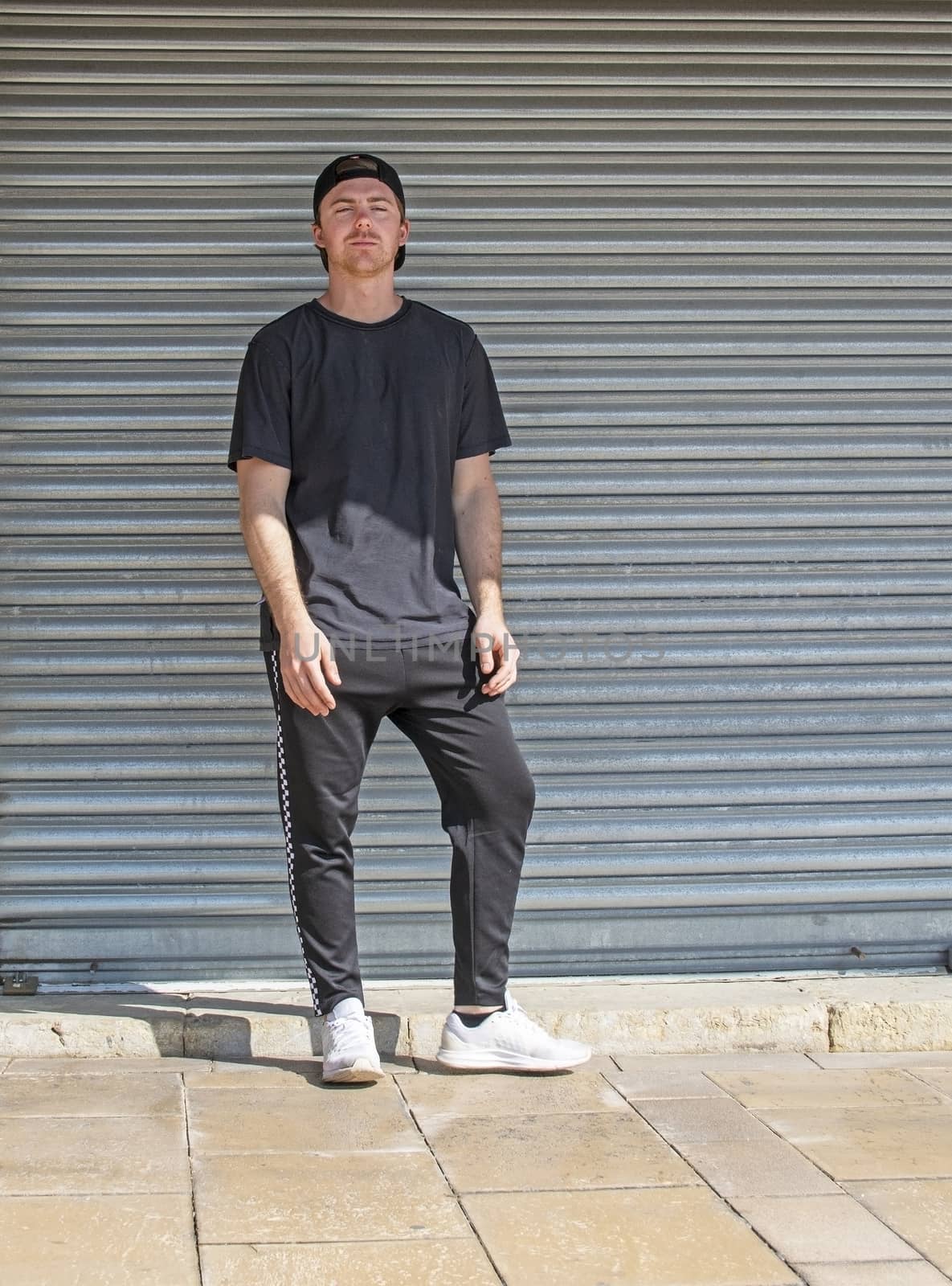 Young casual sporty dressed man with cap backwards in black against corrugated iron wall street style