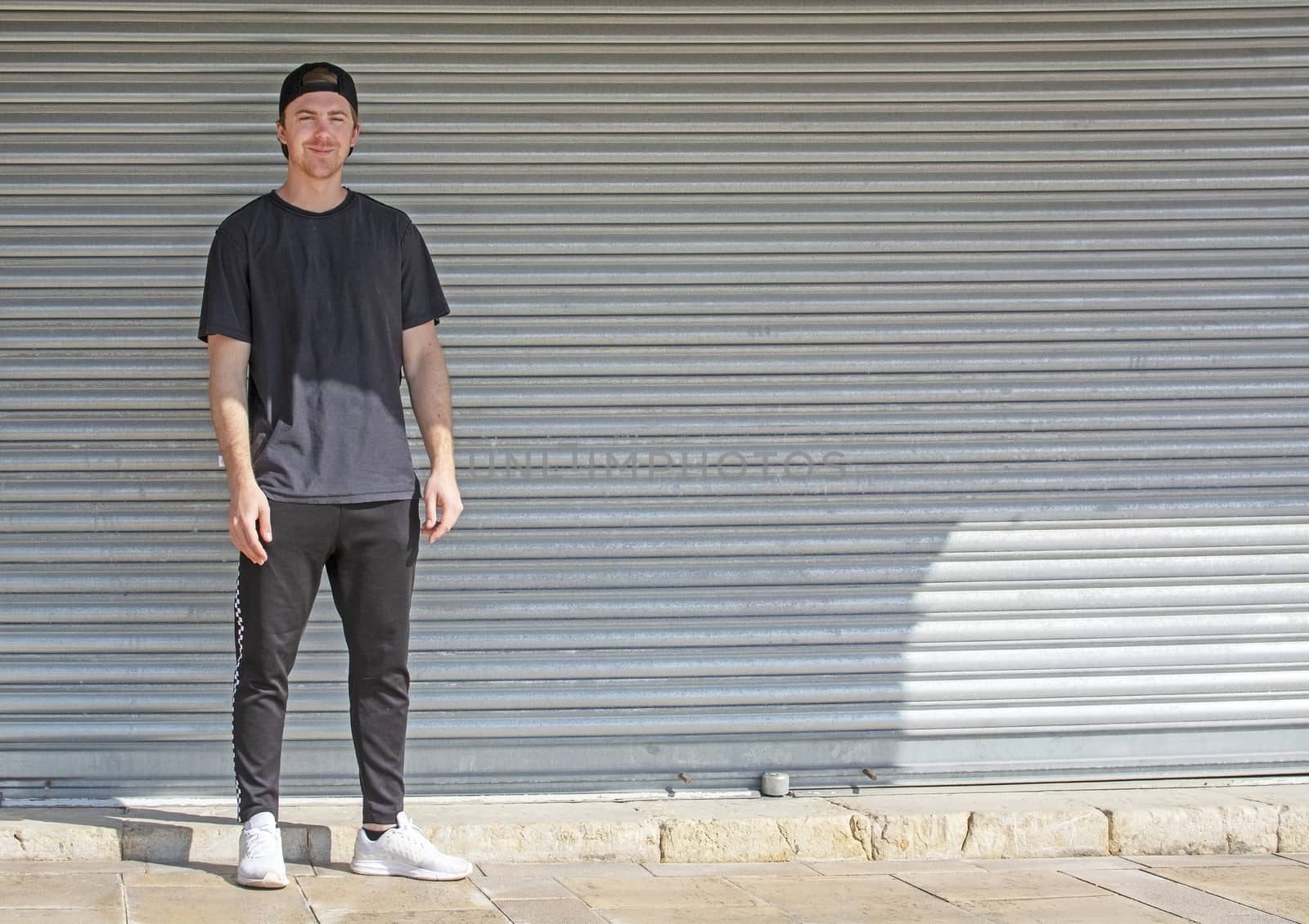 Young casual sporty dressed man with cap backwards in black against corrugated iron wall street style