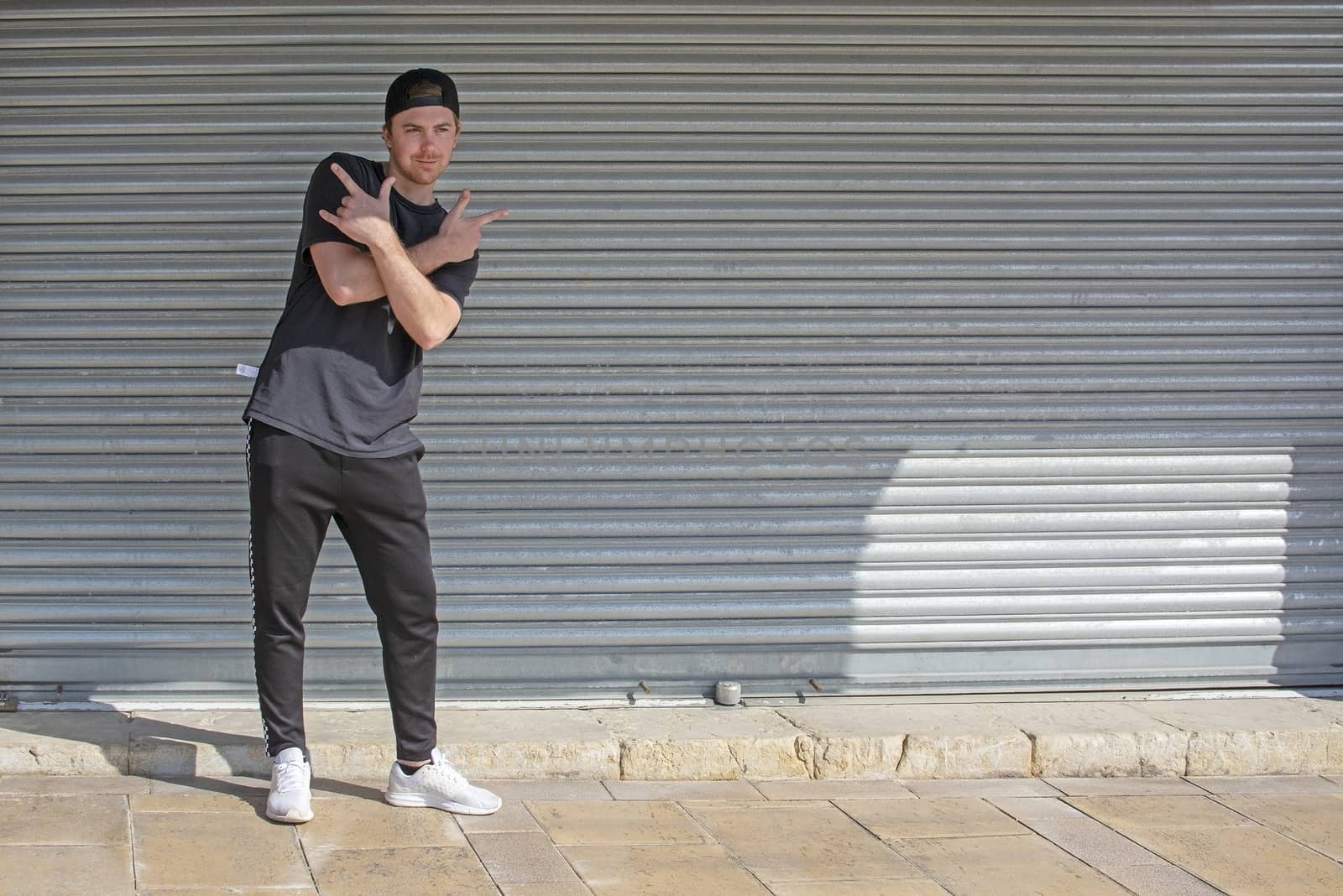 Young casual sporty dressed man with cap backwards in black against corrugated iron wall street style